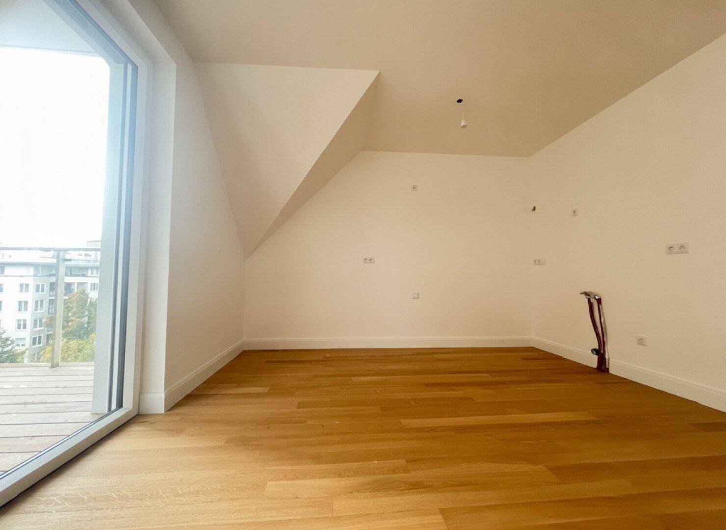 Heller, leerer Raum mit Holzboden, Dachschräge und großem Zugang zu einem Außenbereich.