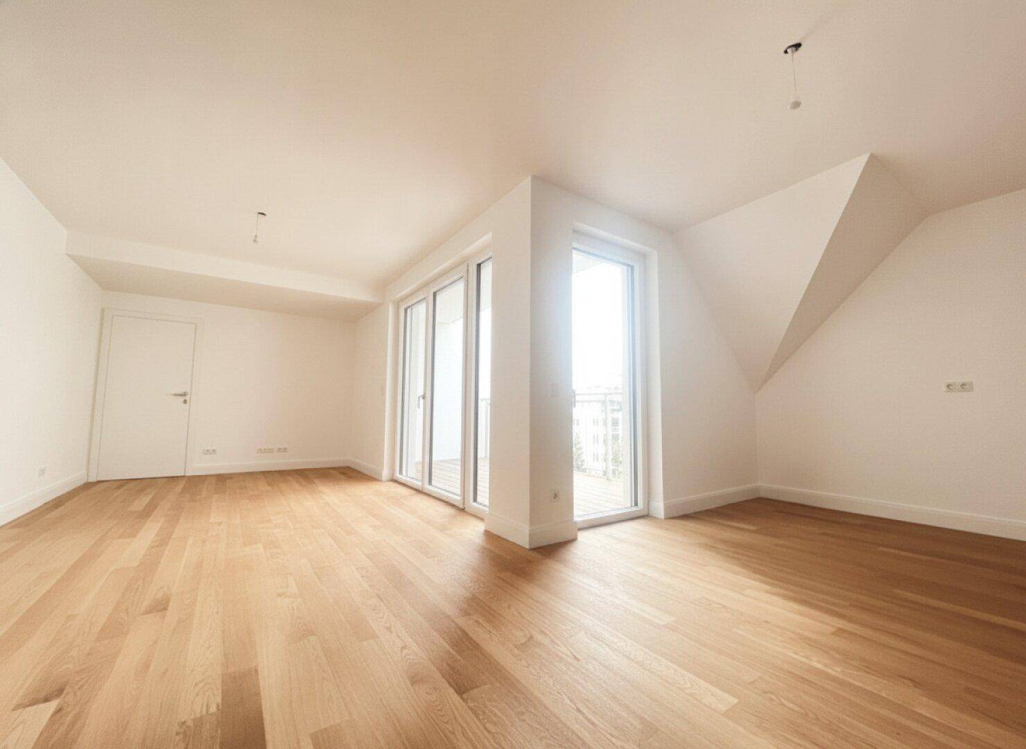 Geräumiger, heller Raum mit Parkettboden, Dachschräge und mehreren Fenstertüren zum Balkon.