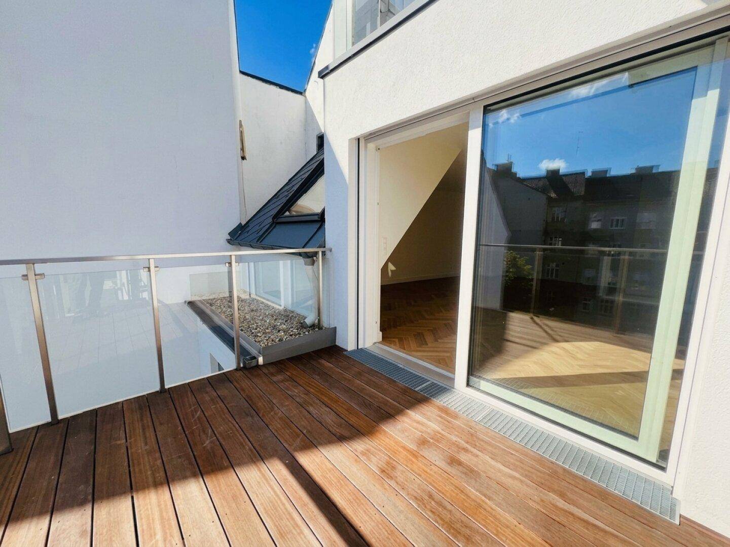 Balkon mit Holzboden und Zugang zu einem hellen Innenraum mit Parkett.