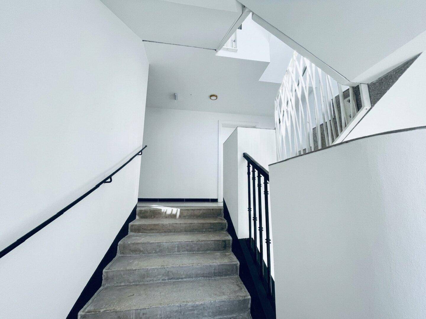 Treppenhaus mit Betonstufen, weiß gestrichenen Wänden und modernem Geländer.