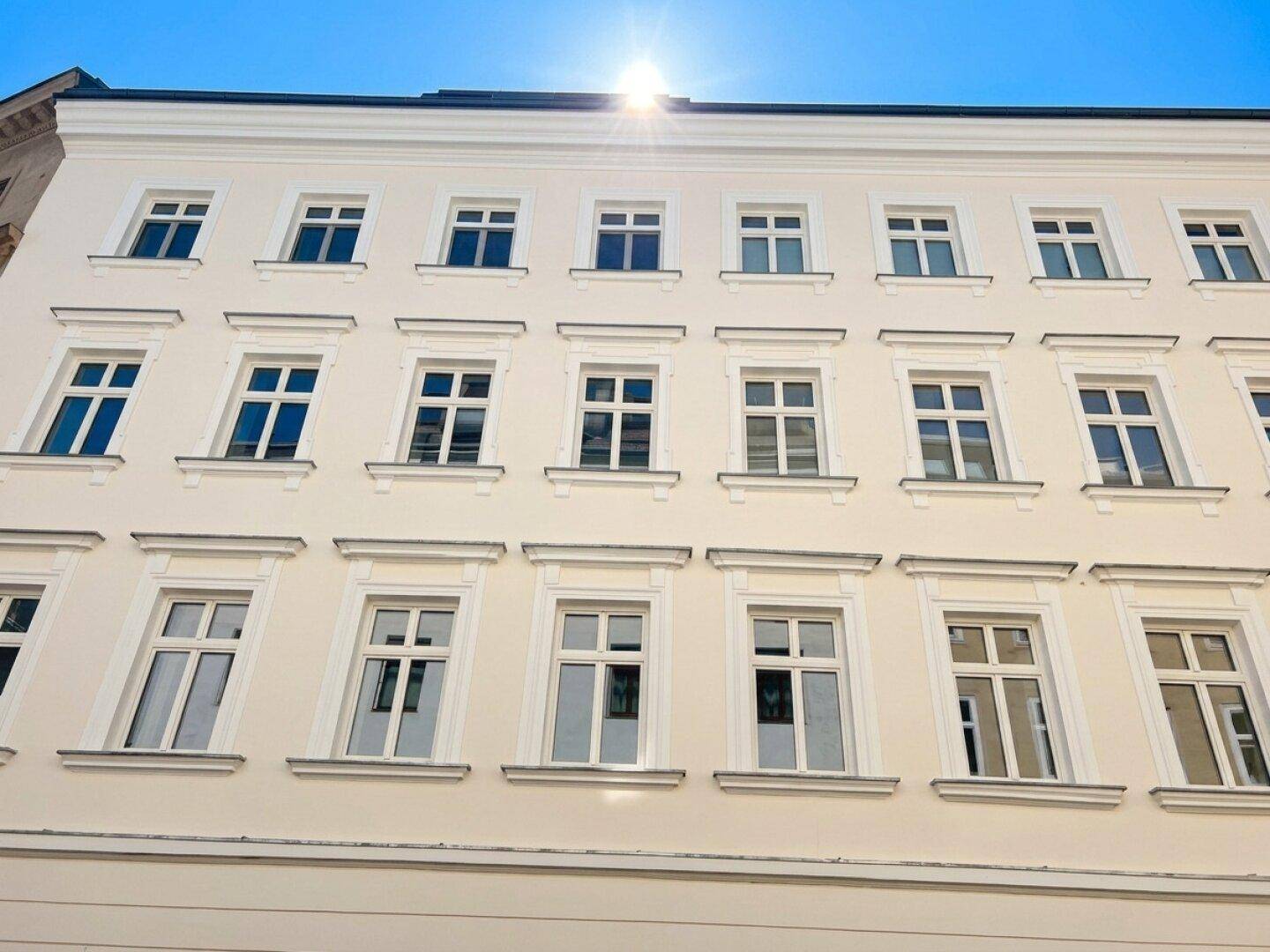 Klassische Fassade eines Mehrfamilienhauses mit vielen Fenstern und hellem Anstrich.
