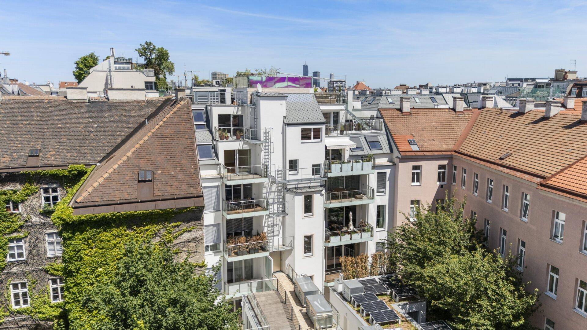 Luftaufnahme eines modernen Wohngebäudes mit mehreren Balkonen und Dachterrassen.