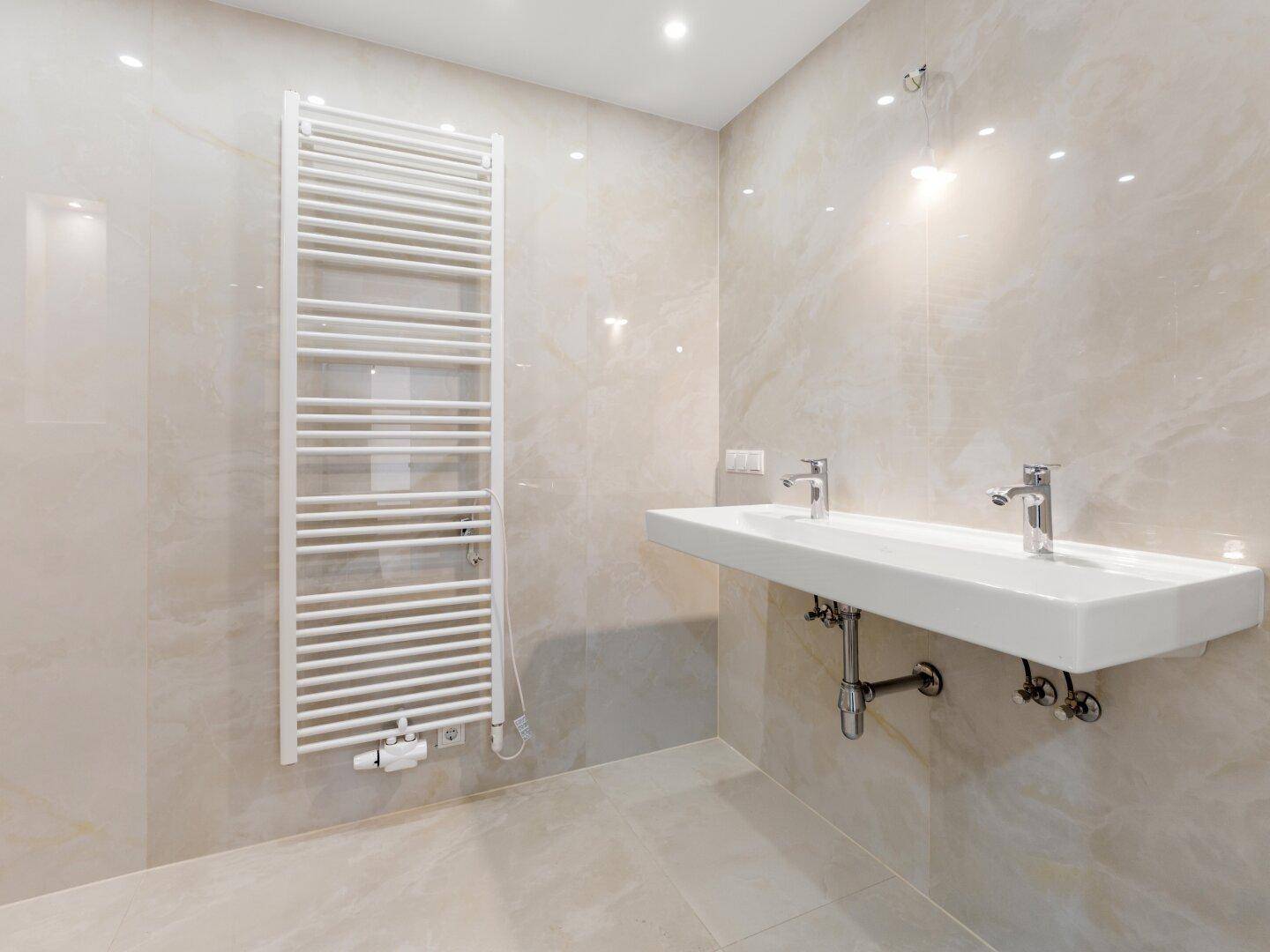 Modernes Badezimmer mit doppelten Waschbecken, beigefarbenen Fliesen und Handtuchheizkörper.