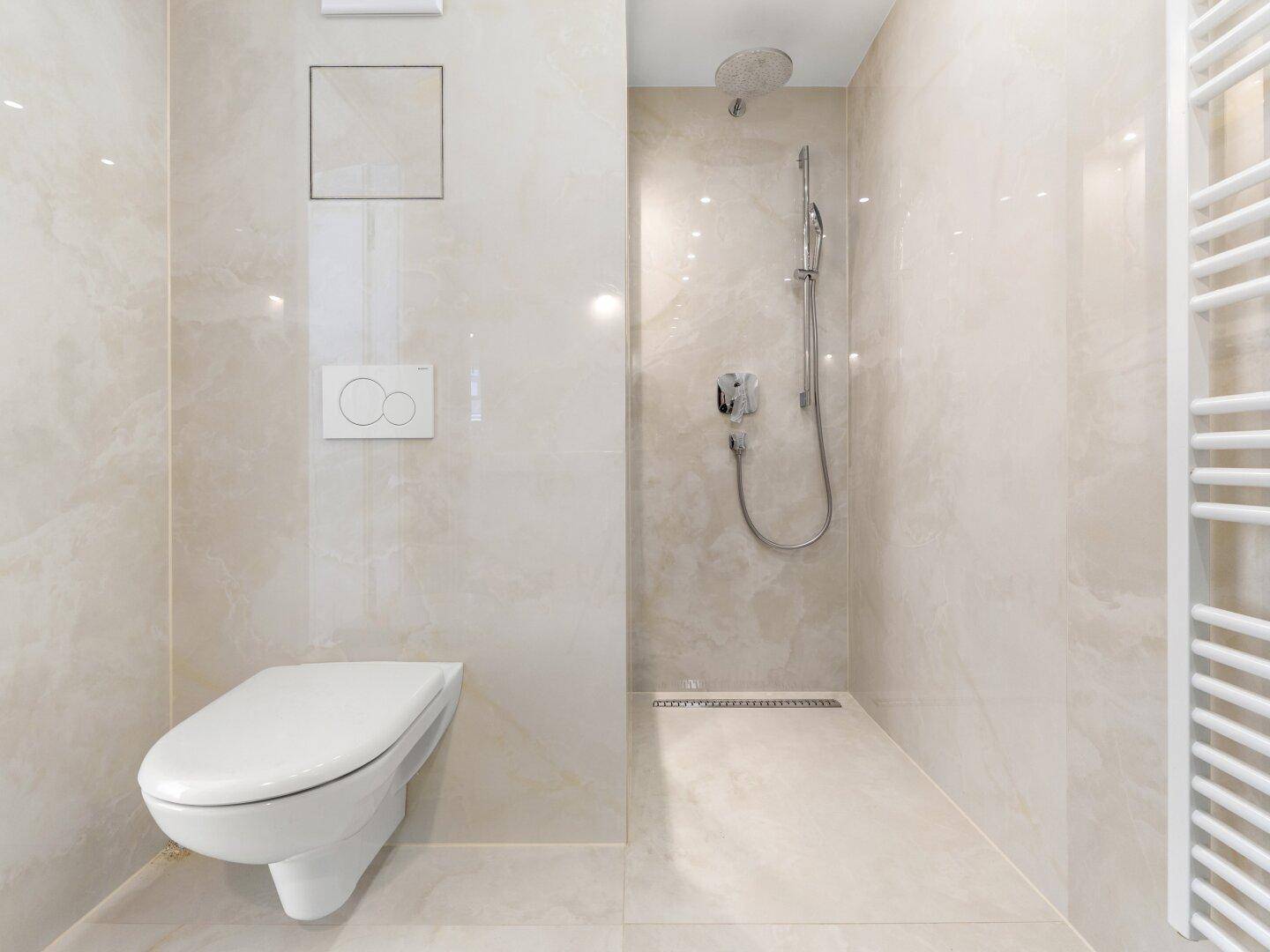 Modernes Badezimmer mit wandhängendem WC, ebenerdiger Dusche und beigefarbenen Fliesen.