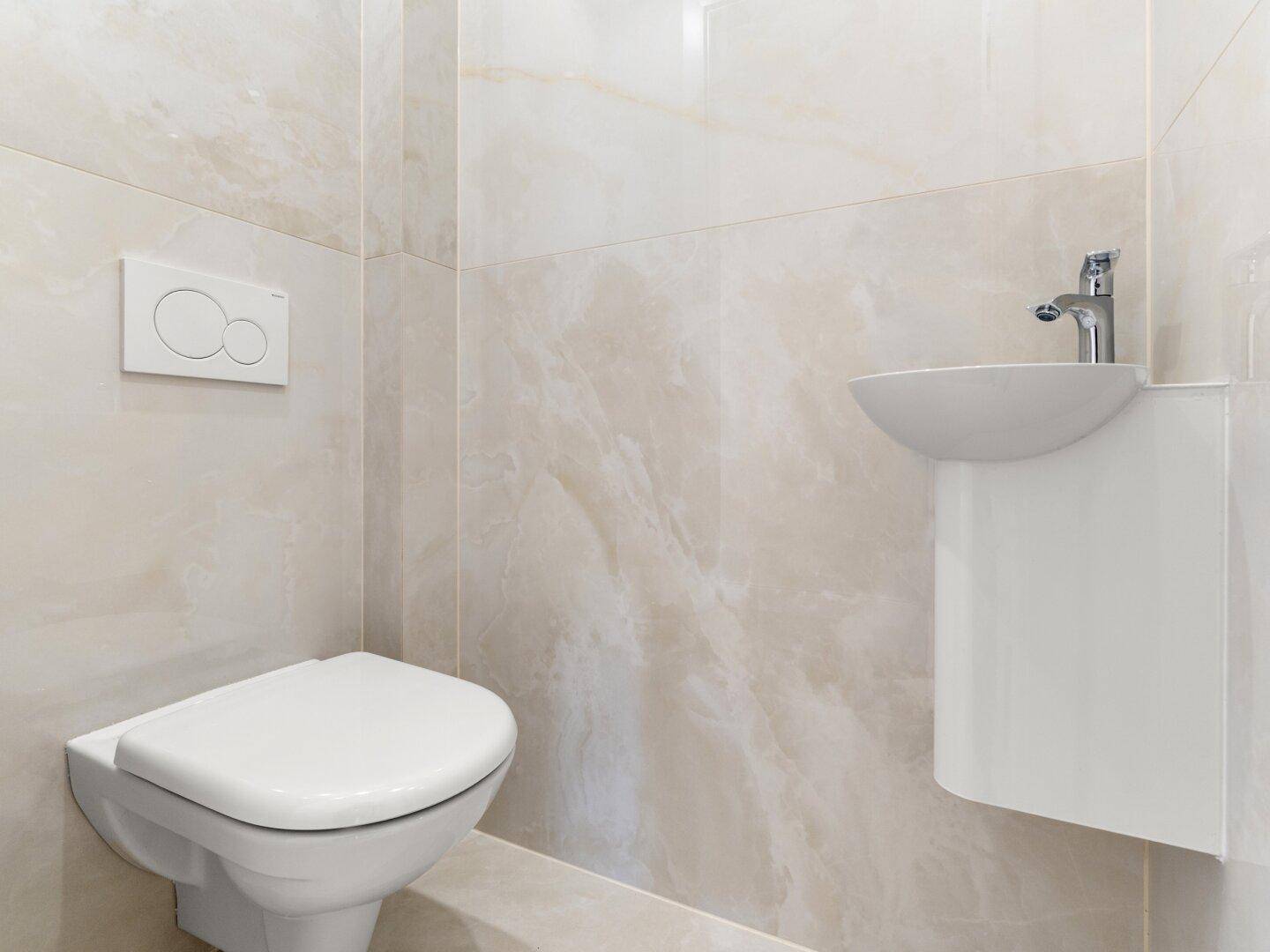 Modernes Gäste-WC mit wandhängendem WC, kleinem Waschbecken und beigefarbenen Fliesen.