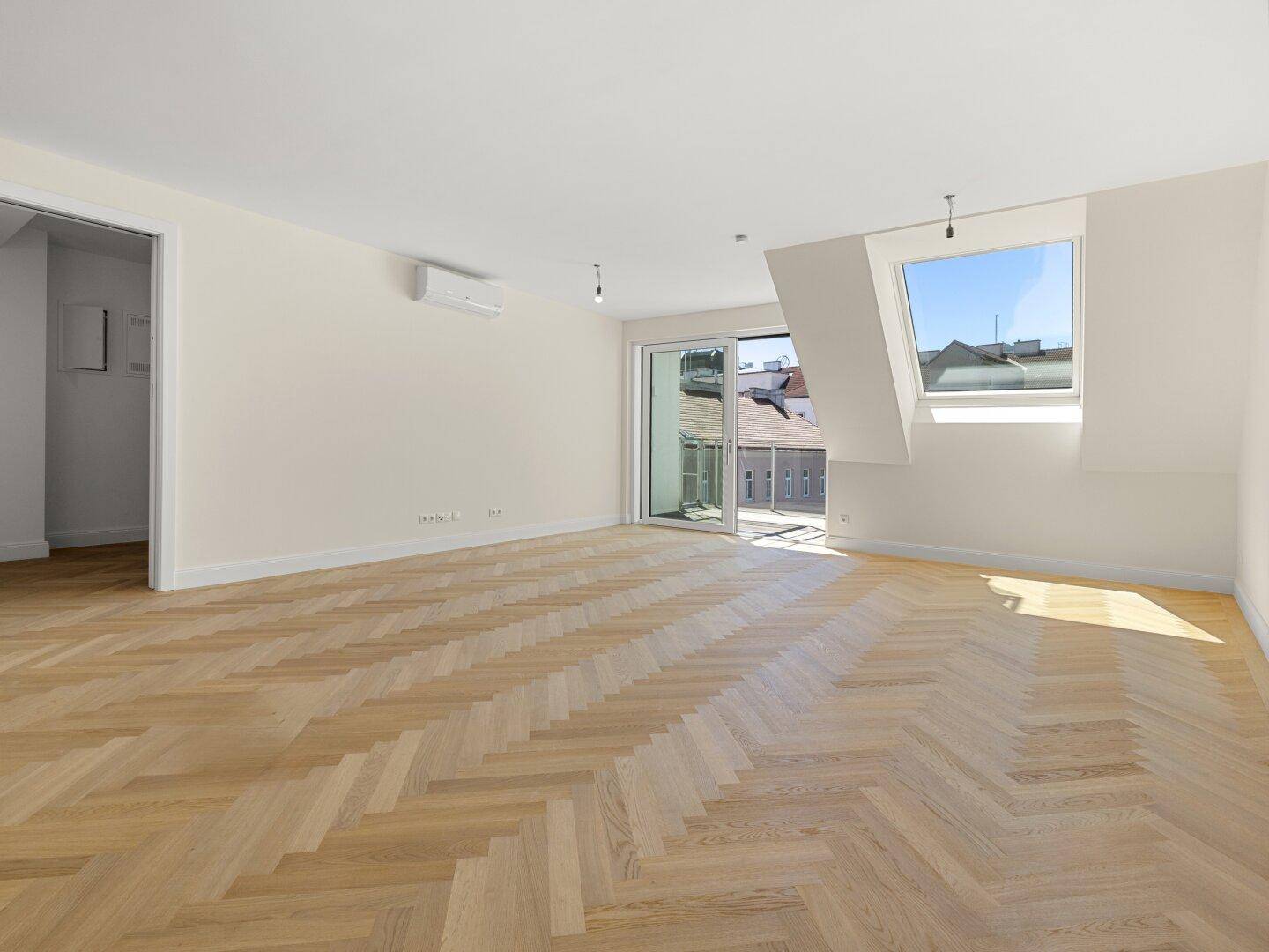 Geräumiges Wohnzimmer mit Dachschrägen, Parkettboden und großen Fenstern.