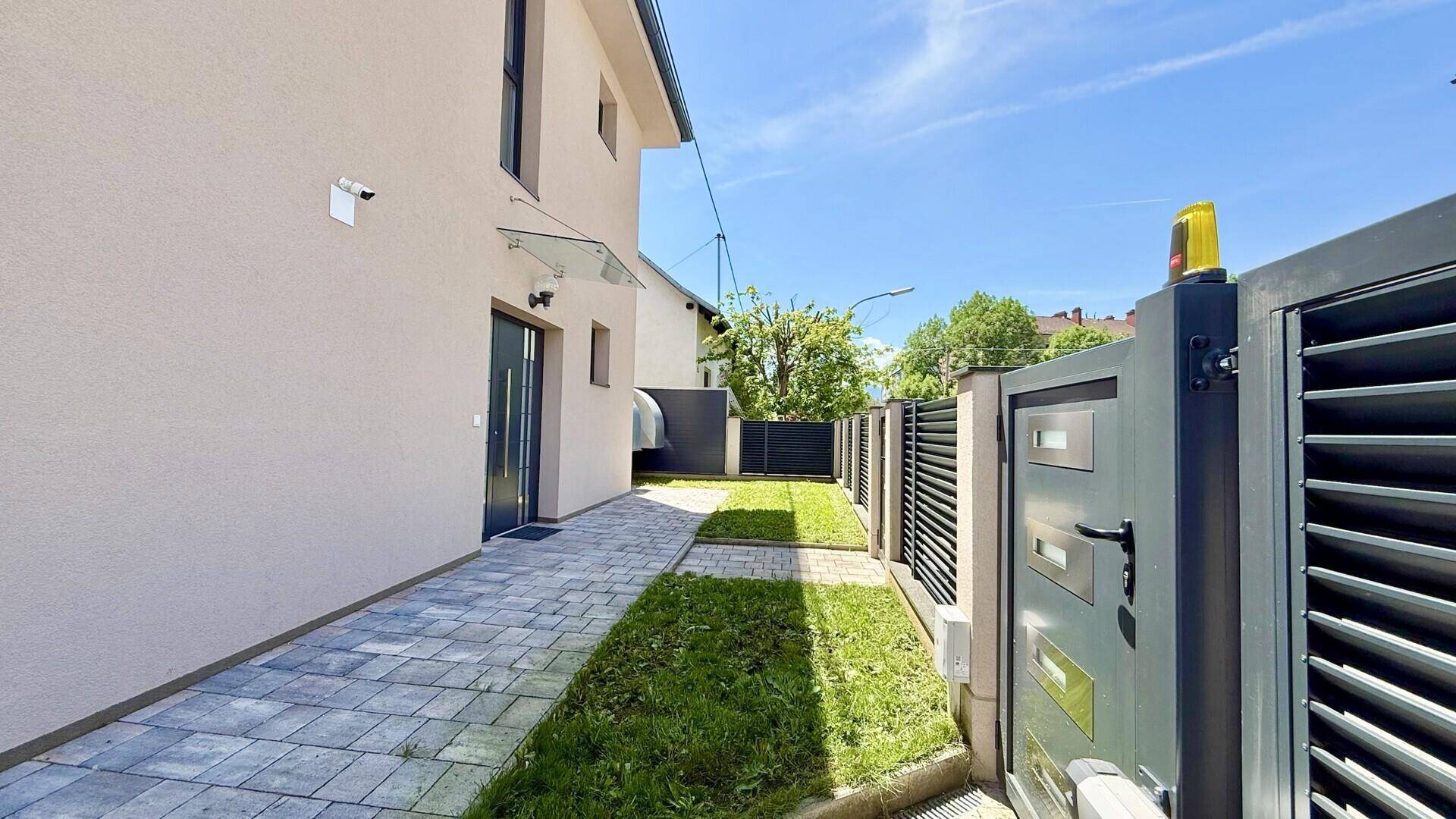 Eingangsbereich des Hauses mit gepflastertem Weg, Rasenstreifen und modernem Metalltor.