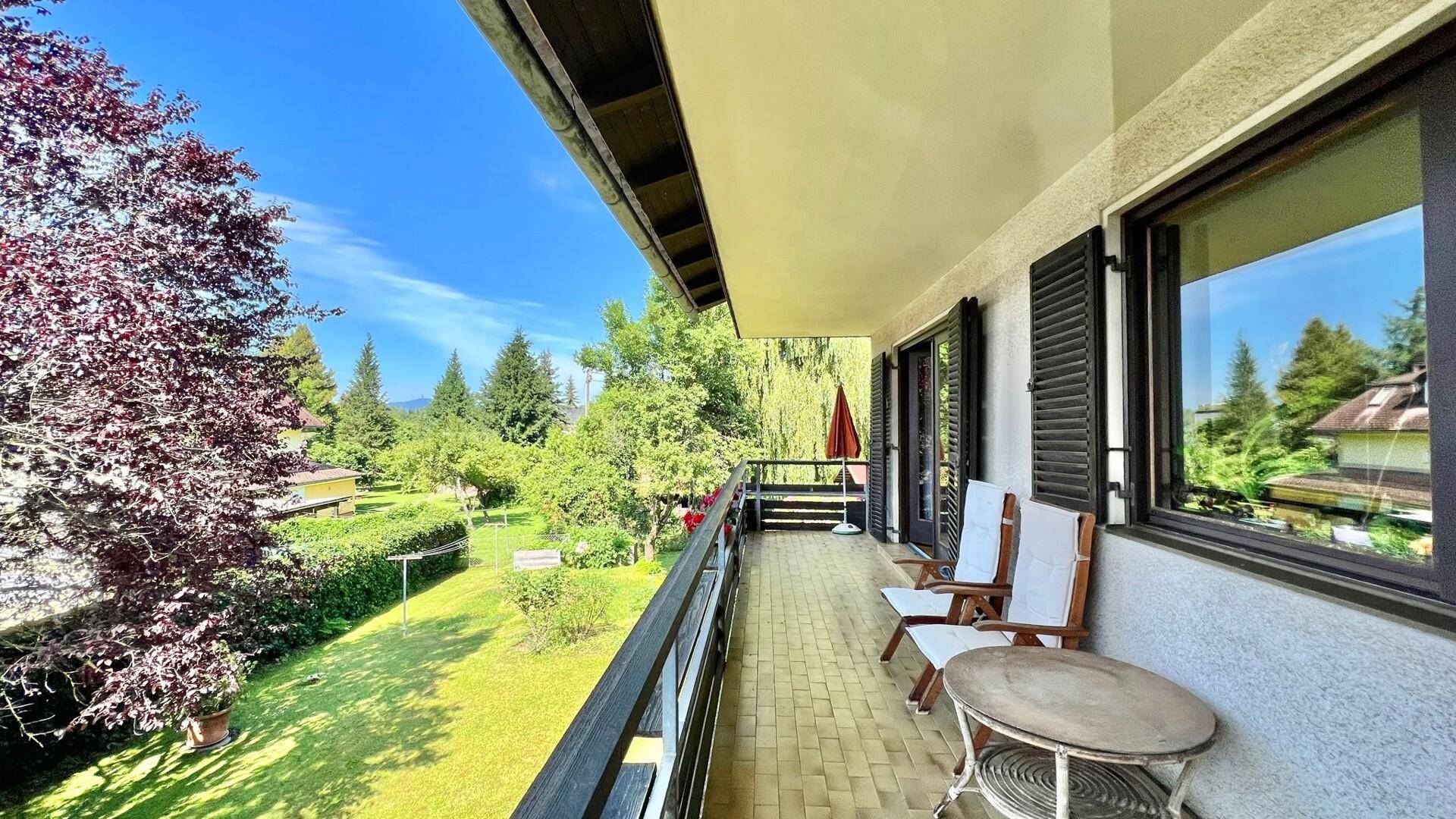 Geräumiger Balkon mit Fliesenboden und Sitzgelegenheiten, umgeben von viel Grün.