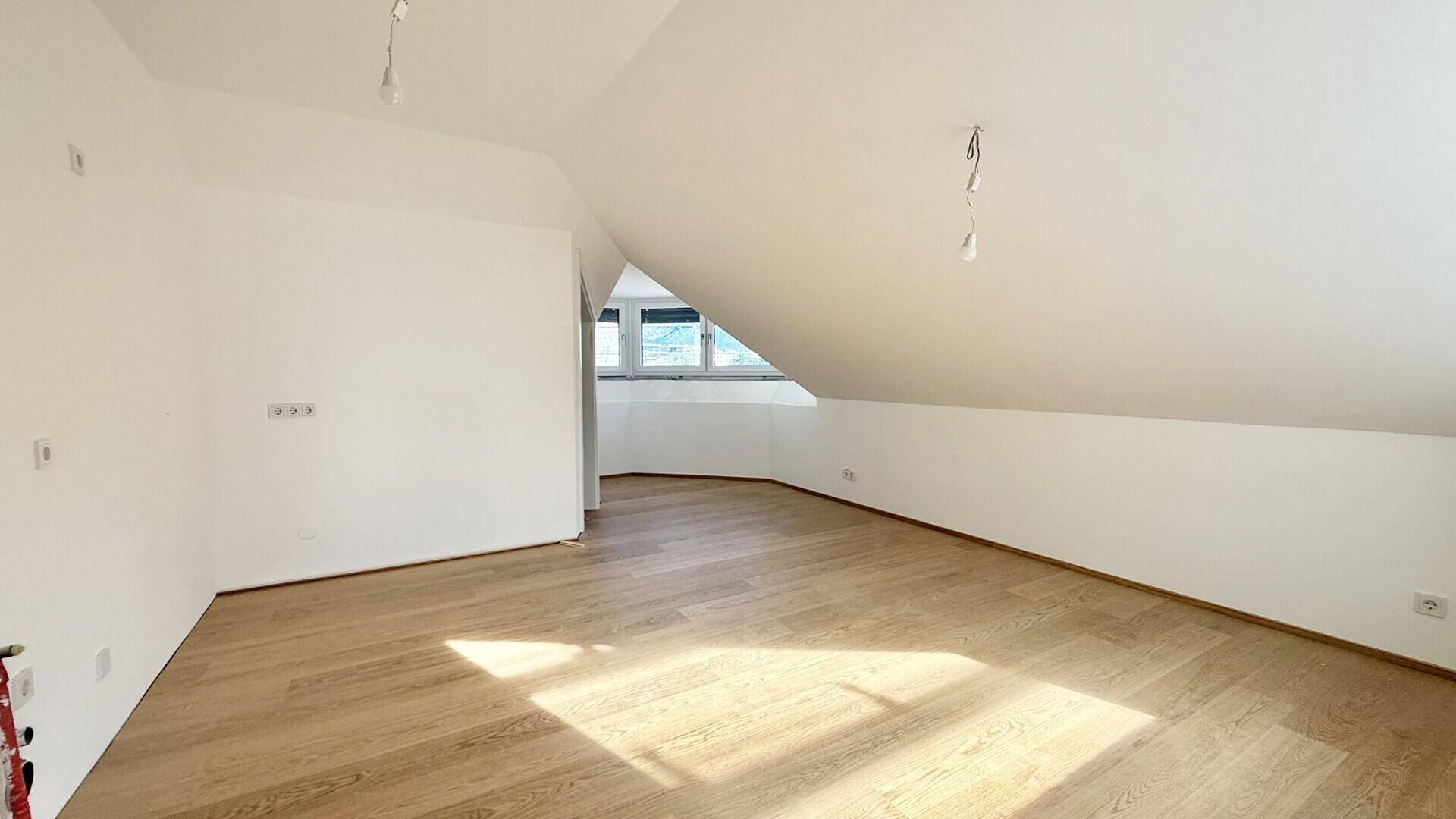 Heller, leerer Raum im Dachgeschoss mit Holzboden und schrägen Wänden.