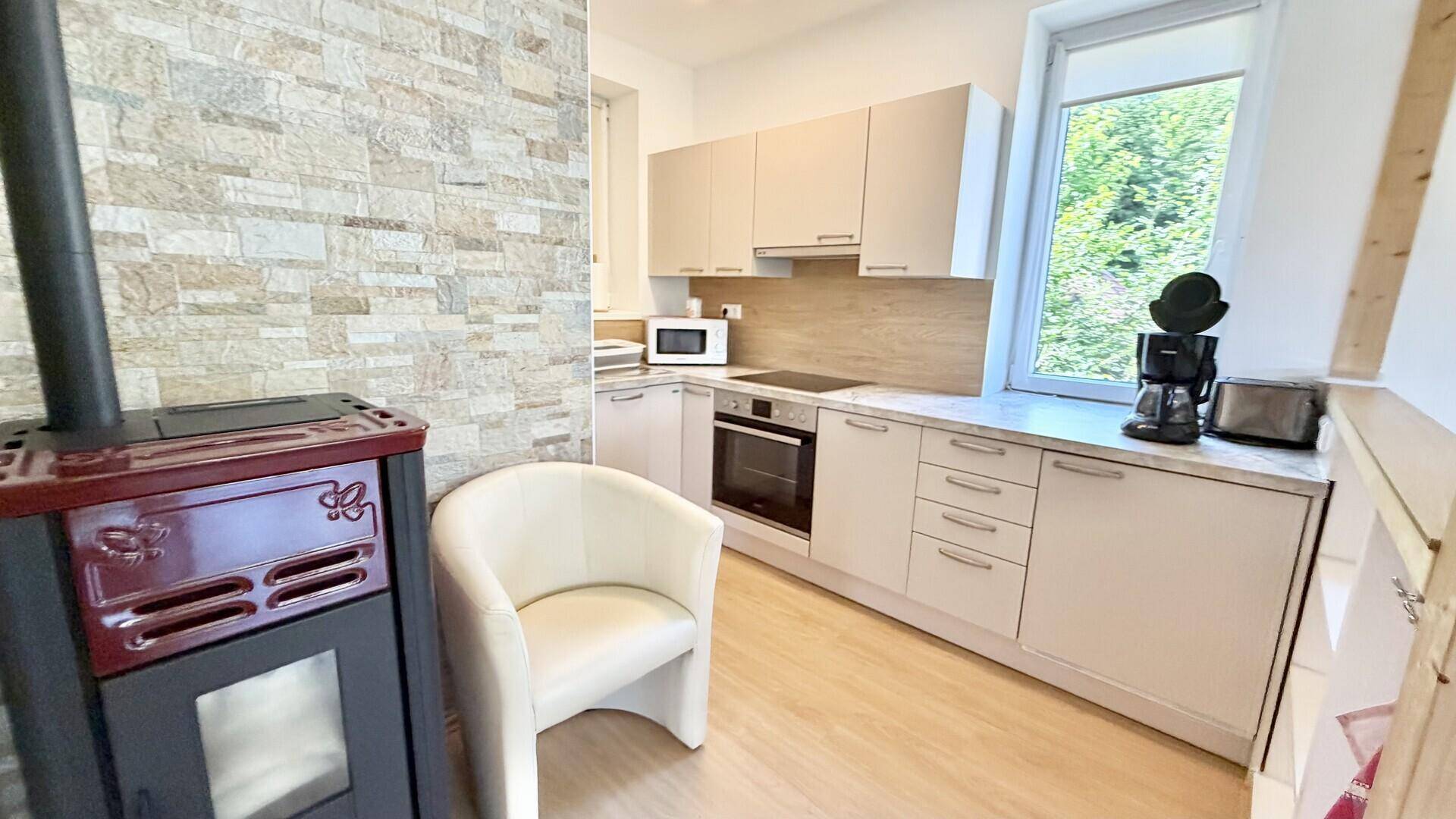 Funktionale Küche mit hellen Schränken, Steinwand und einem modernen Kaminofen im Vordergrund.