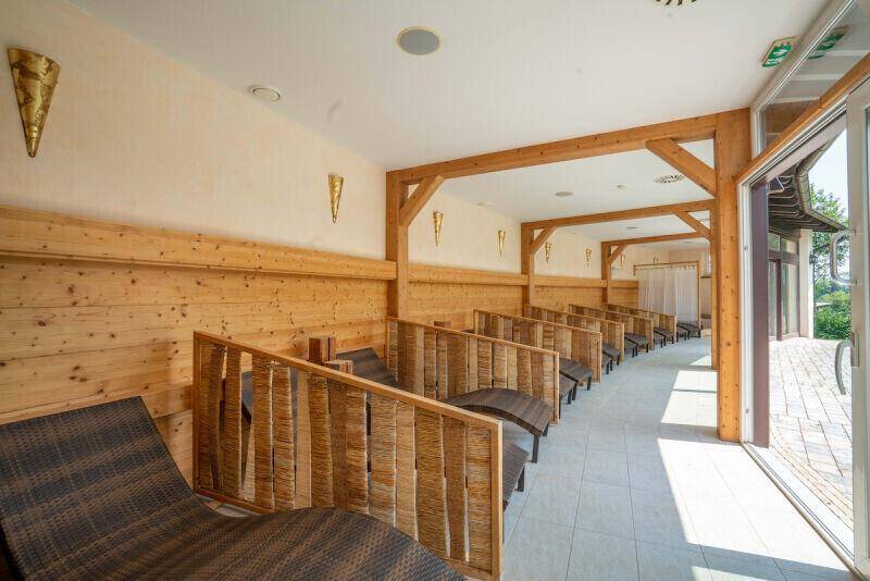 Entspannungsbereich mit Holzverkleidung, bequemen Liegen und großen Fenstern zum Außenbereich, bietet Ruhe und Komfort.