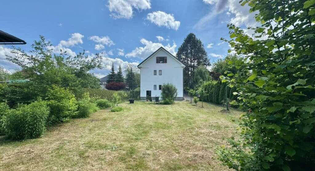 Weitläufiger Garten hinter dem Haus mit großer Rasenfläche und üppiger Vegetation.