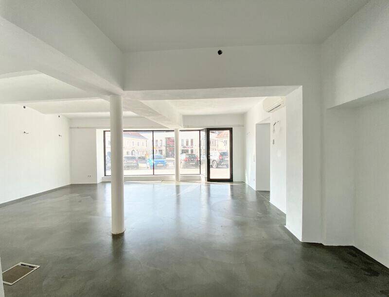 Großer, heller Geschäftsraum mit Säulen, Betonboden und breiten Schaufenstern.