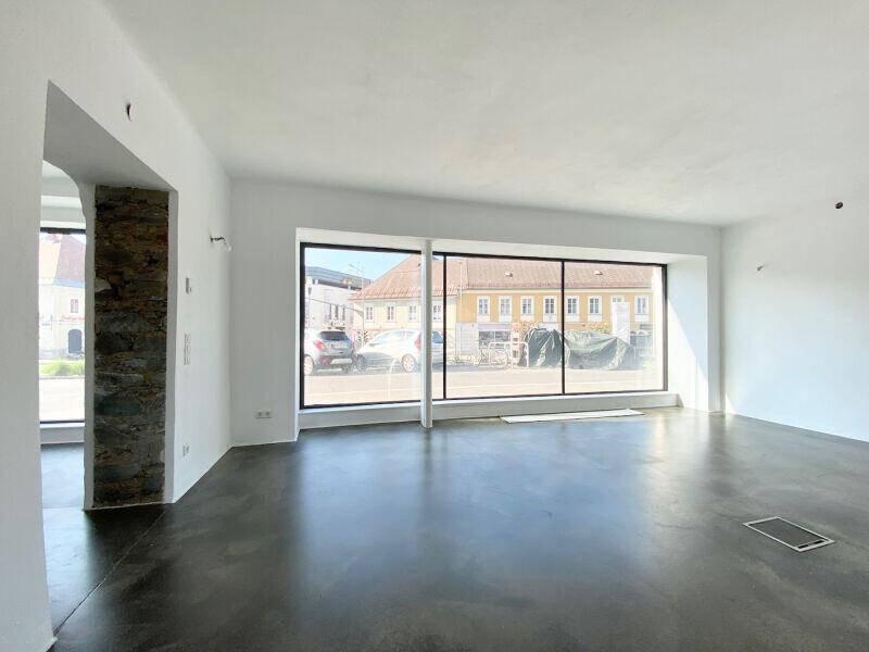 Offener Geschäftsraum mit großen Fenstern, Betonboden und einer dekorativen Steinwand.