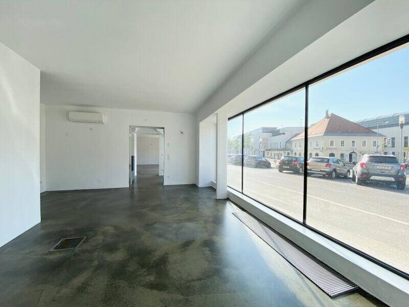 Heller, leerer Geschäftsraum mit großen Schaufenstern und Blick auf die belebte Straße.
