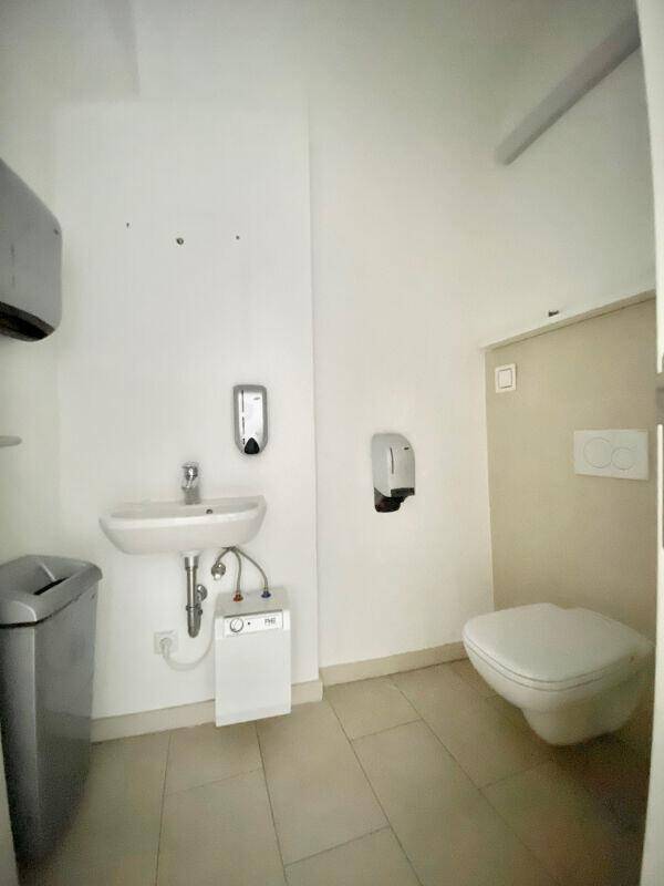 Sauberes WC mit wandhängender Toilette, Waschbecken und Seifenspendern.