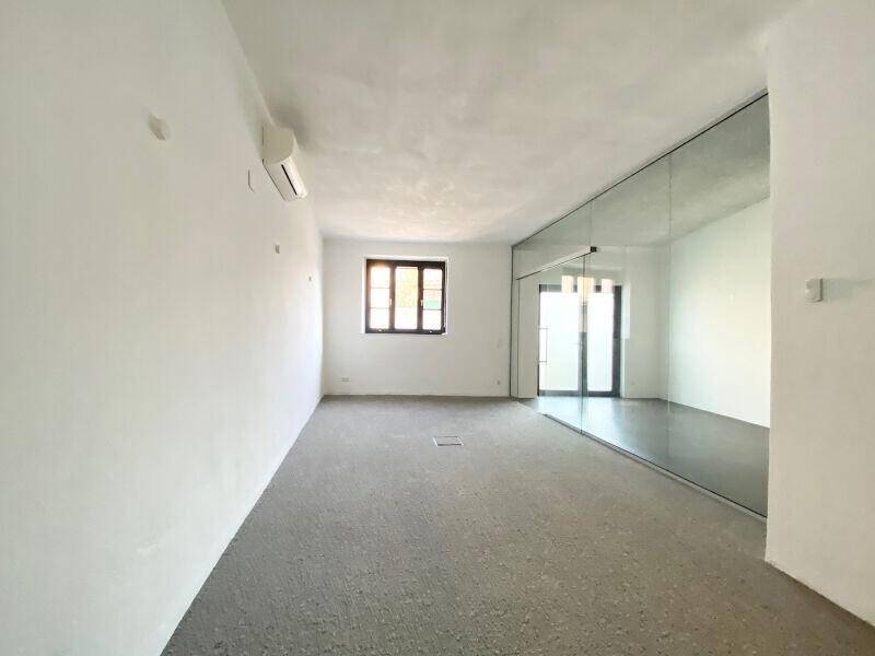 Heller Raum mit Fenster, Teppichboden und einer verspiegelten Wand.