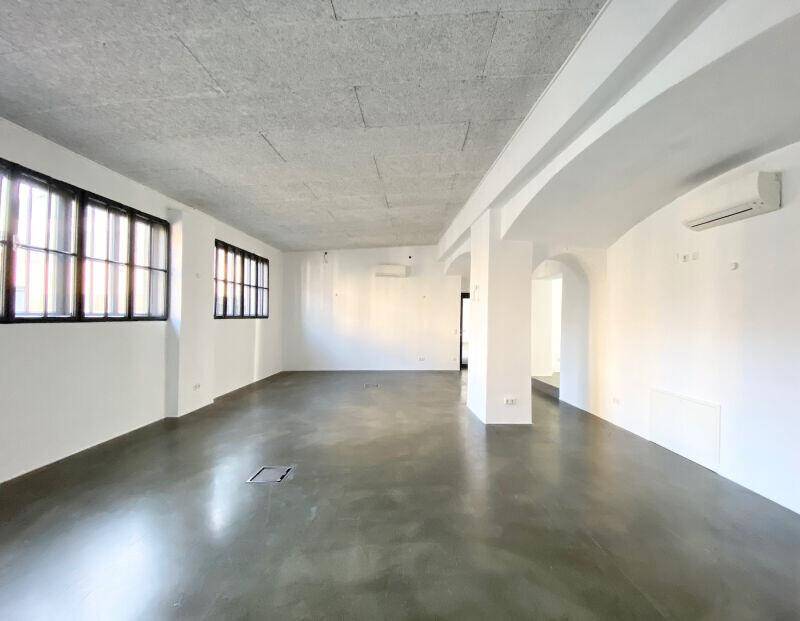 Großer, offener Raum mit hohen Decken, großen Fenstern und Betonboden.