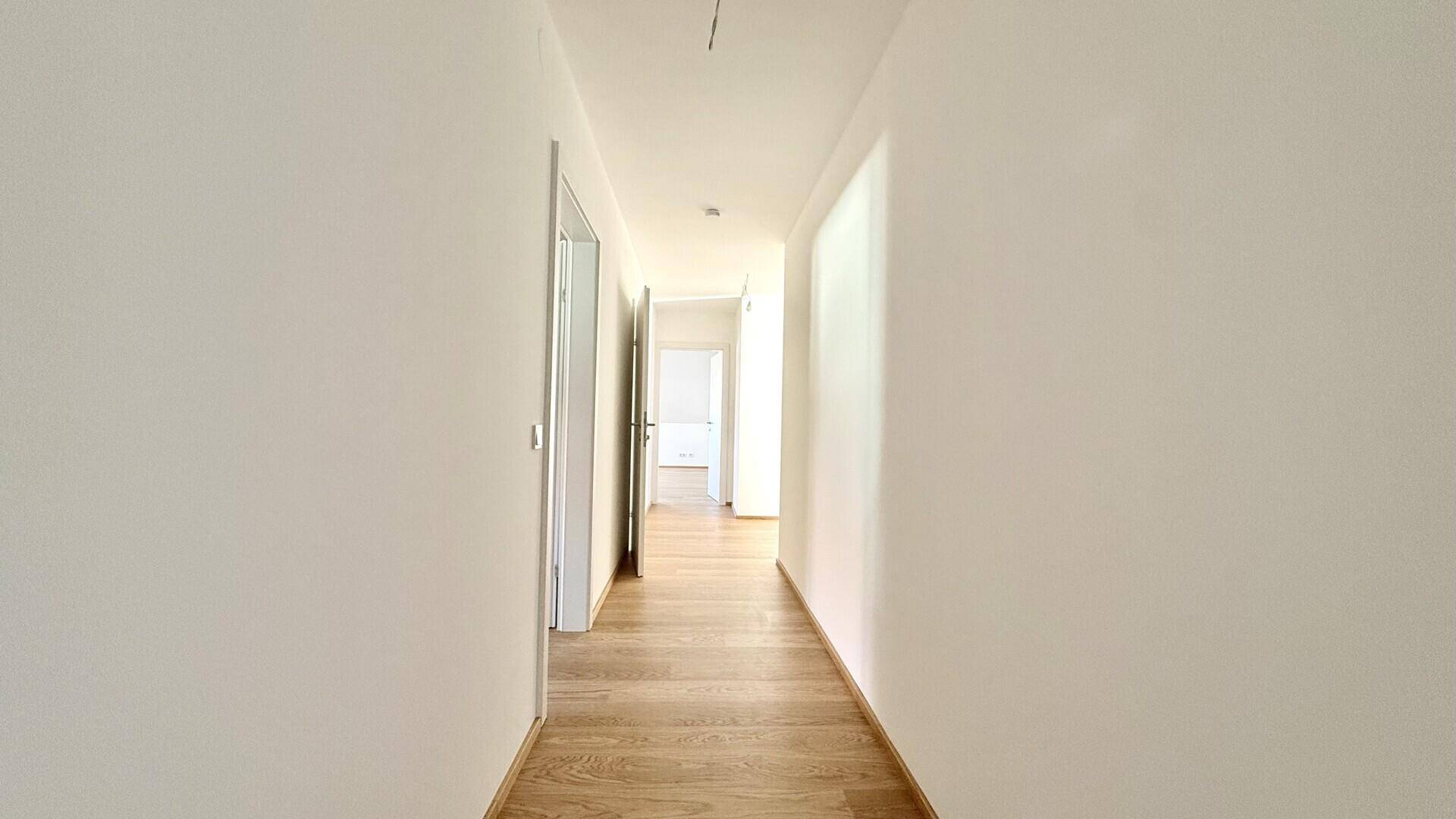 Geräumiger, heller Flur mit Holzboden und weißen Wänden, der zu weiteren Räumen führt.