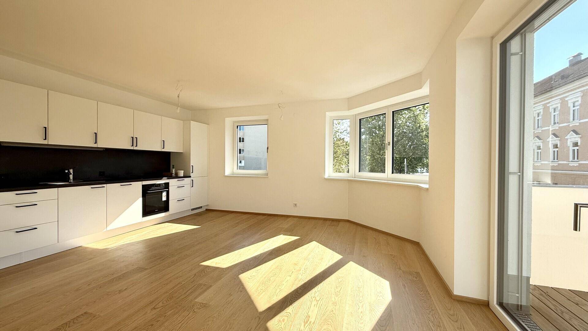Moderne Einbauküche mit weißen Schränken und hellem Holzboden in offenem Wohnbereich.