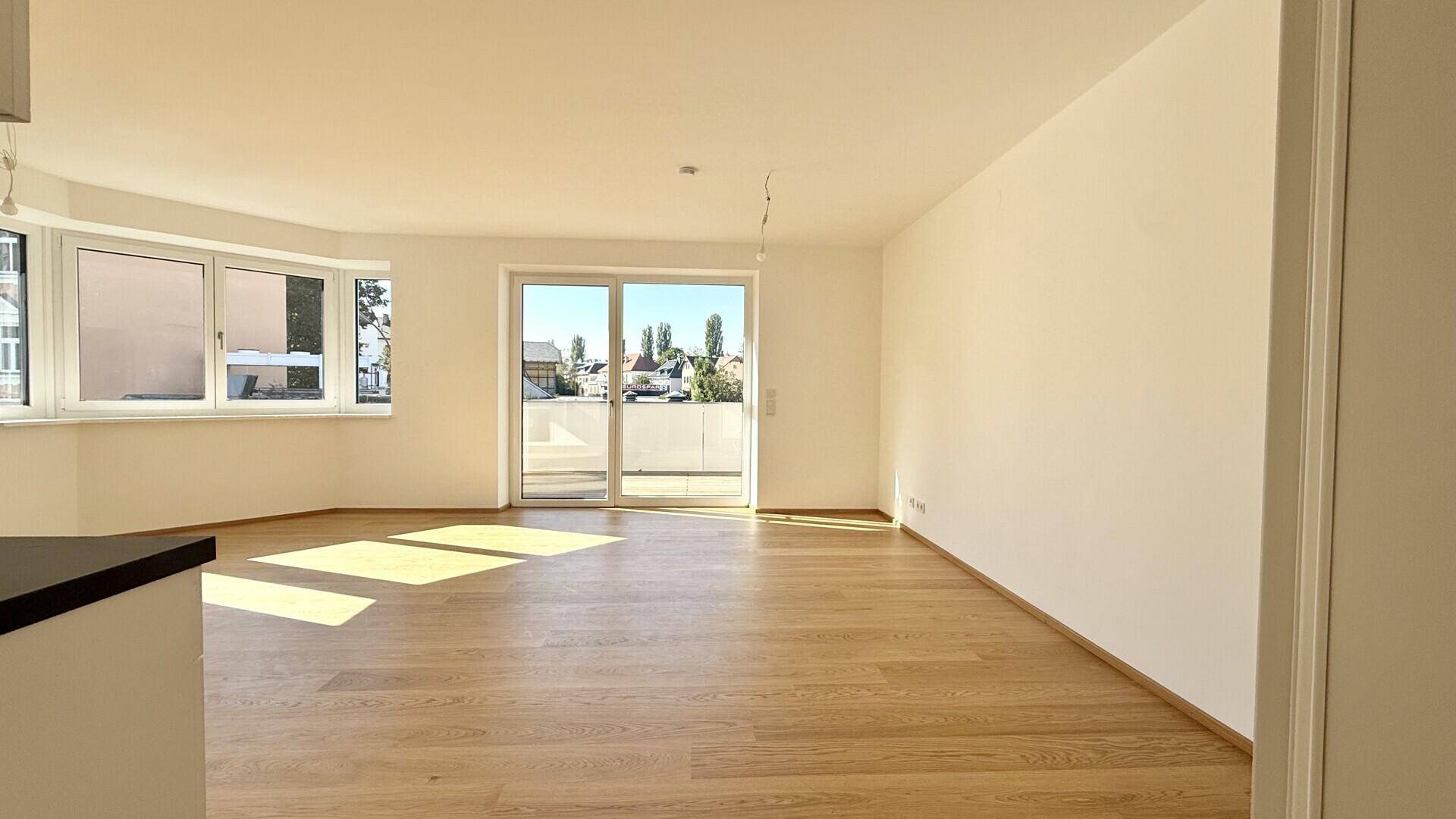 Geräumiger, heller Raum mit Holzboden und Schiebetür zum Balkon.