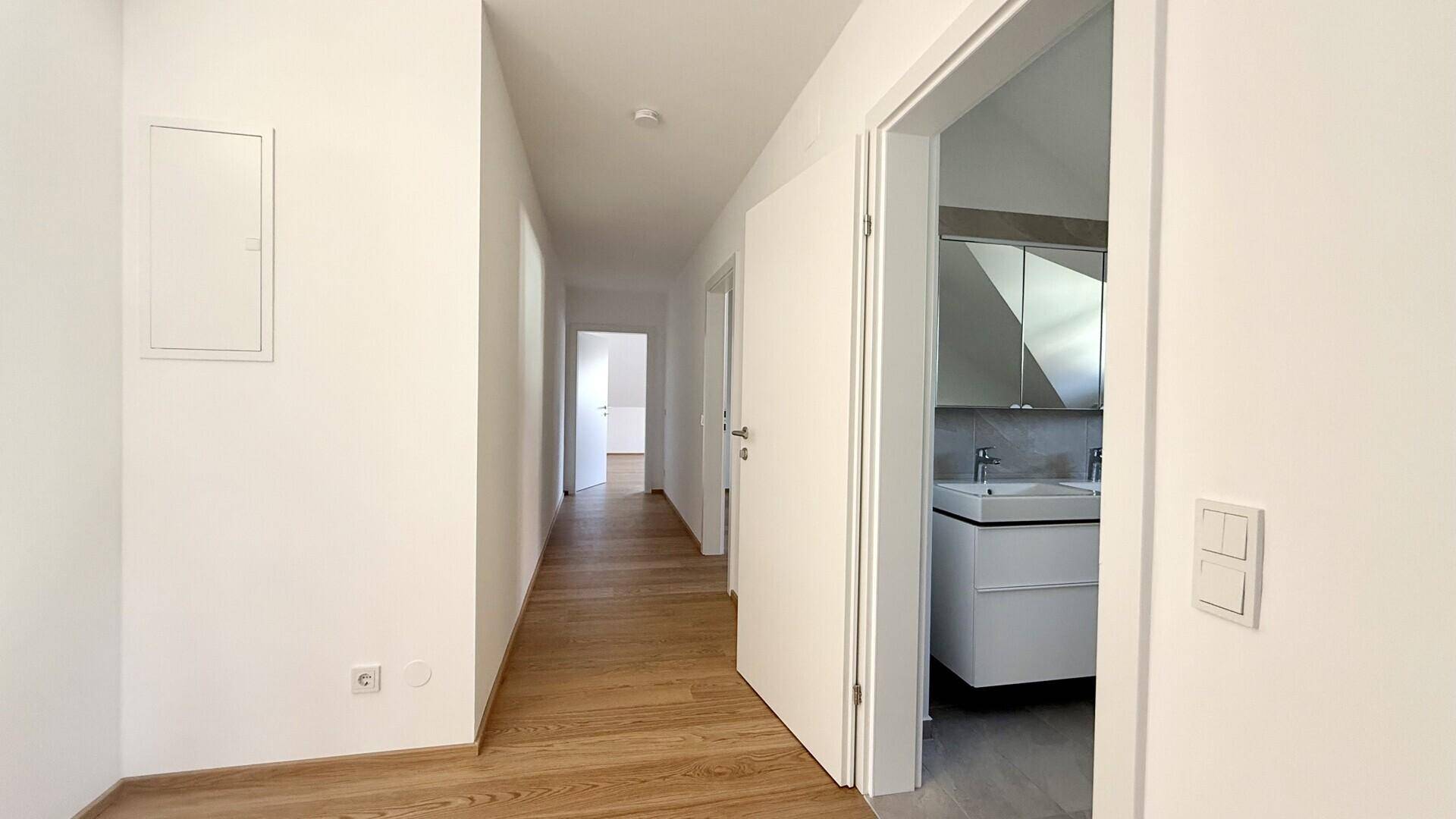 Langer Flur mit Holzboden und Zugang zu einem modernen Badezimmer.