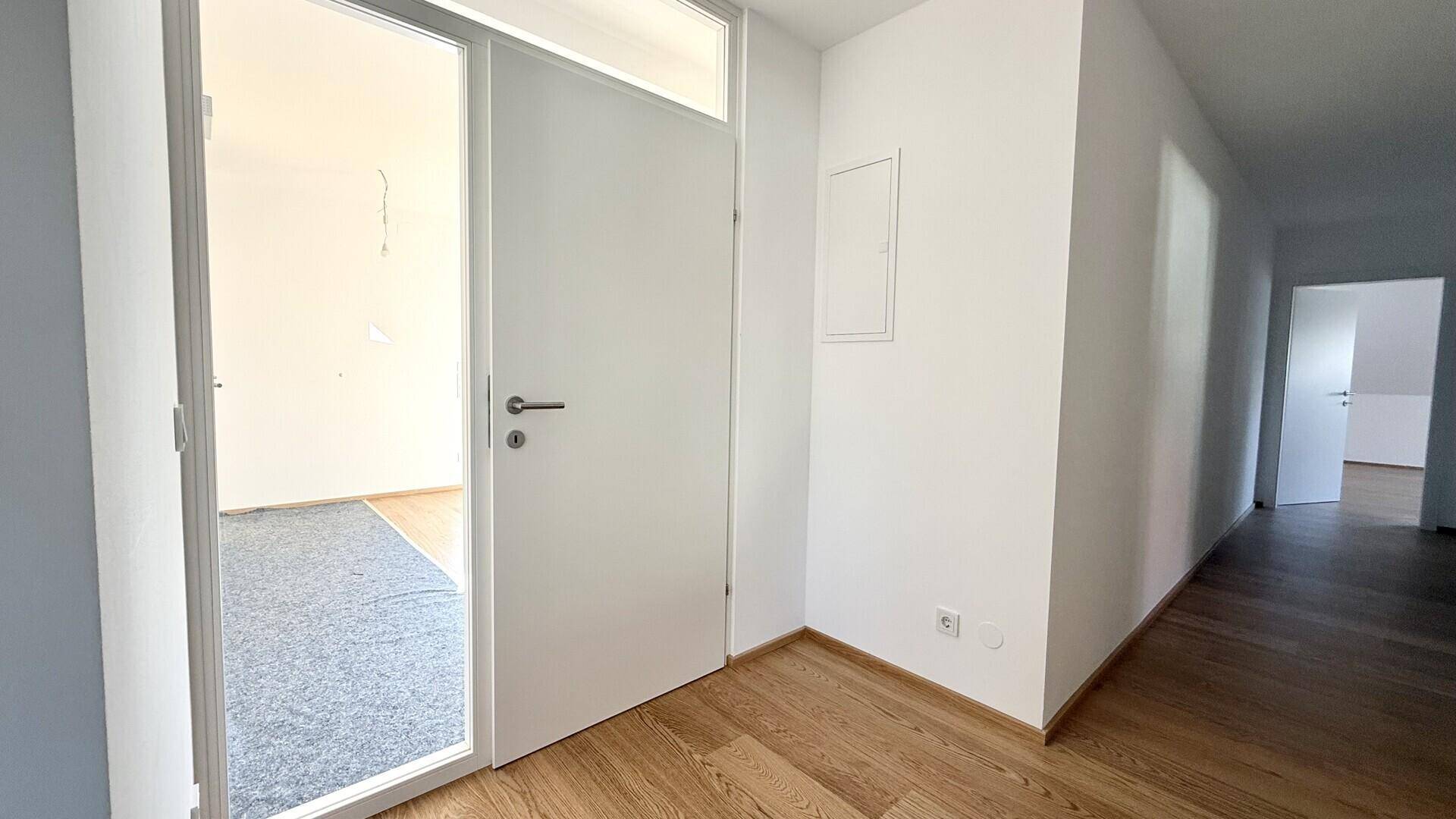 Heller Flur mit Holzboden und weißer Tür, die zu einem weiteren Raum führt.