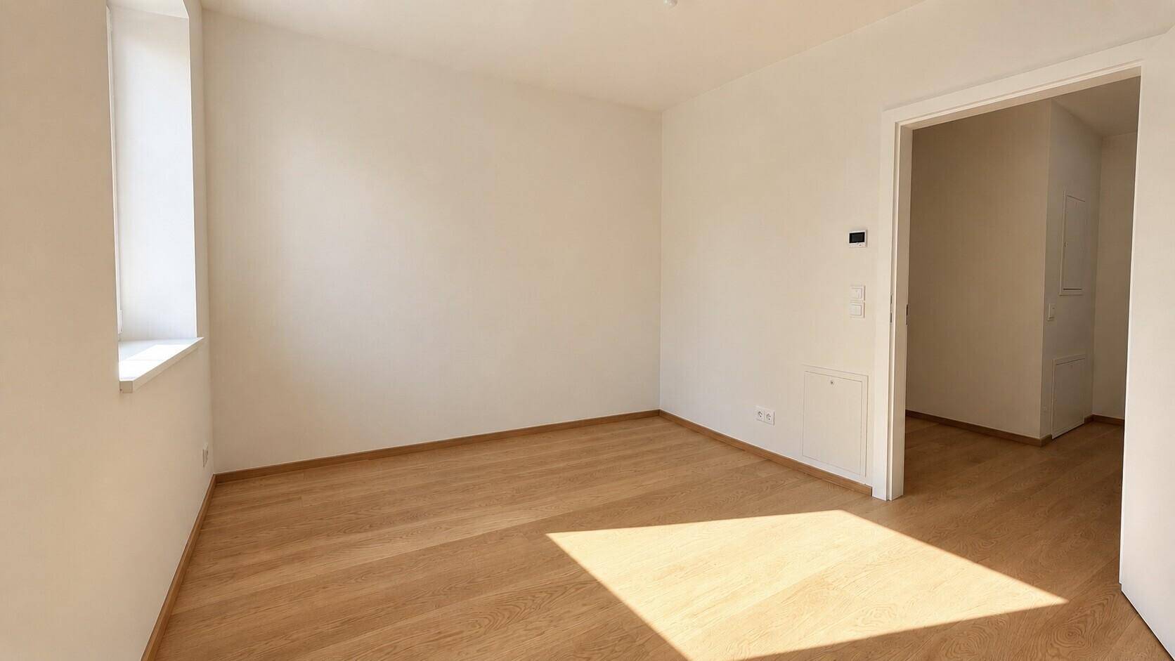 Leeres Zimmer mit Holzboden und Fenster, bereit zur individuellen Gestaltung.
