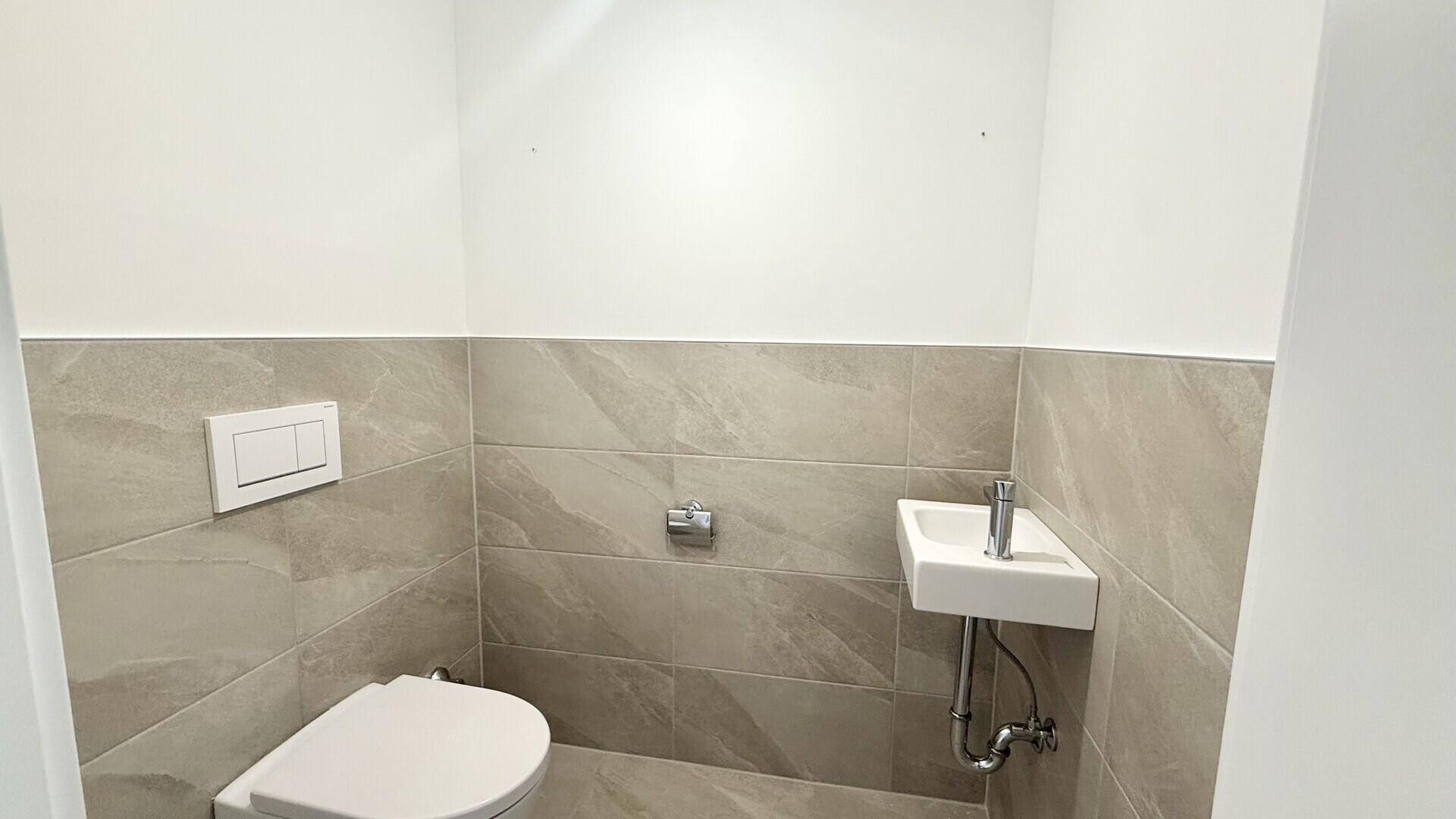 Gäste-WC mit modernen Fliesen, wandhängendem WC und kleinem Handwaschbecken.