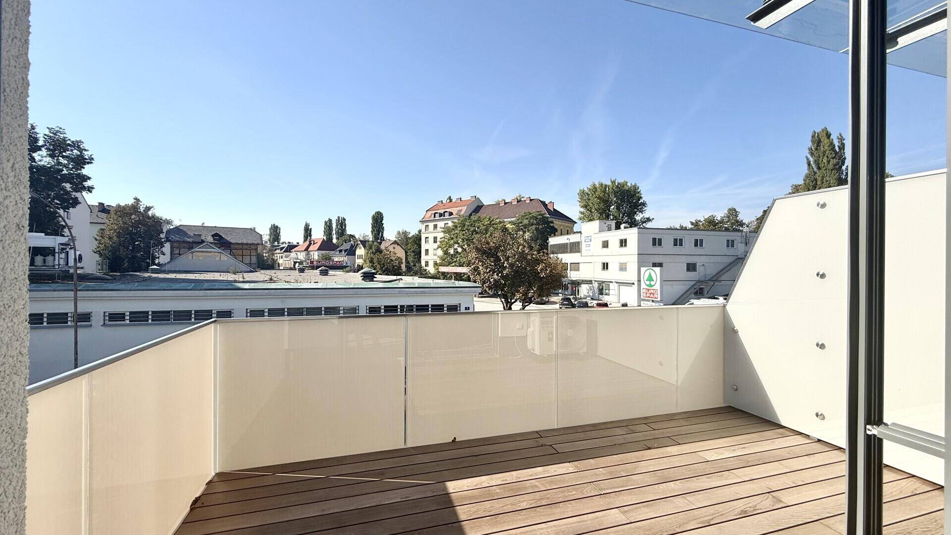 Geräumiger Balkon mit Holzboden und Blick auf die umliegende Bebauung.