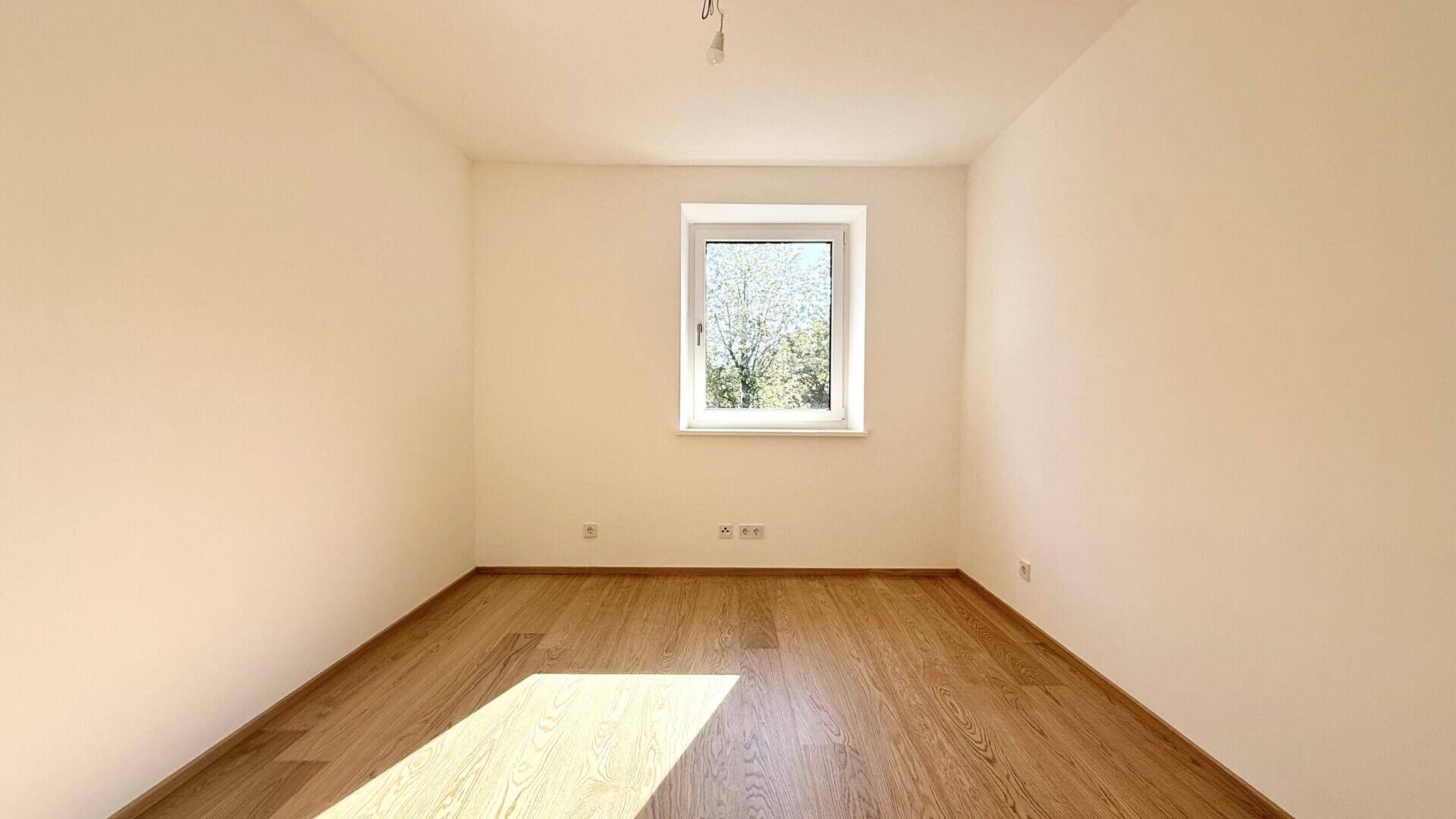 Ruhiges Zimmer mit Holzboden und einem Fenster, das viel Tageslicht hereinlässt.