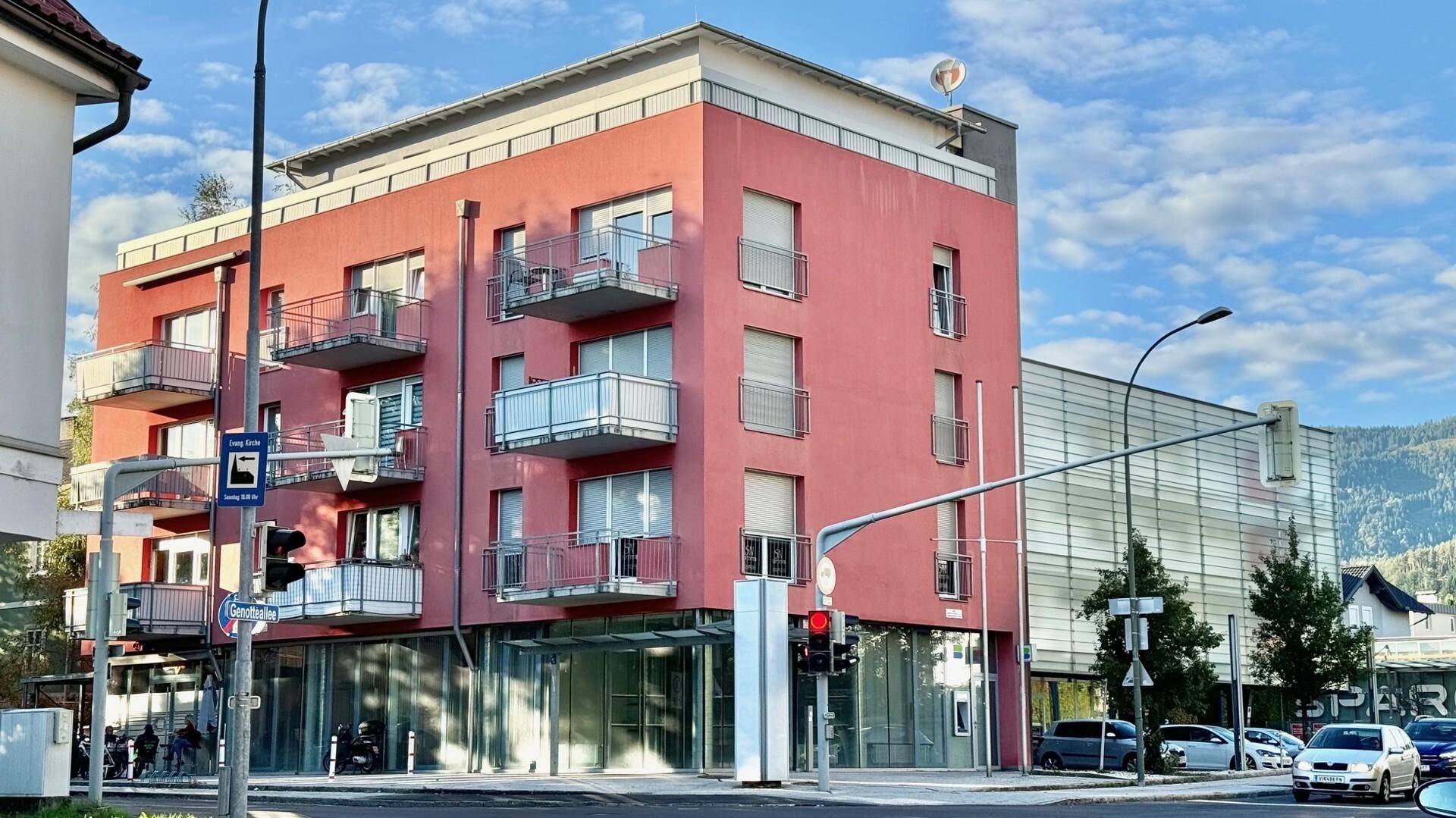 Modernes Gebäude mit roter Fassade, Balkonen und großen Fenstern an einer Straßenecke.