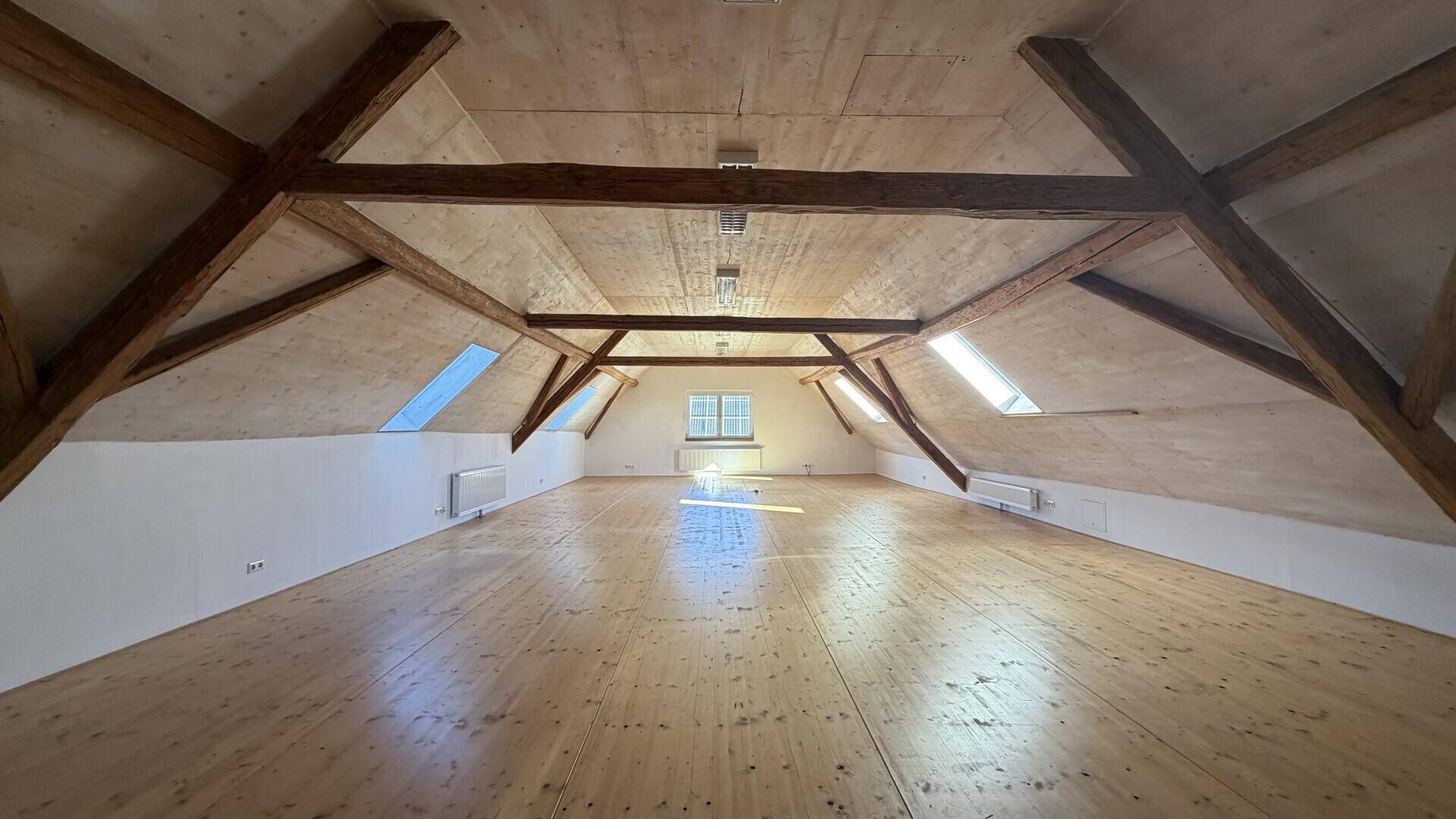 Heller Dachbodenraum mit Holzboden, sichtbaren Dachbalken und Dachfenstern, ideal für Ausbau.