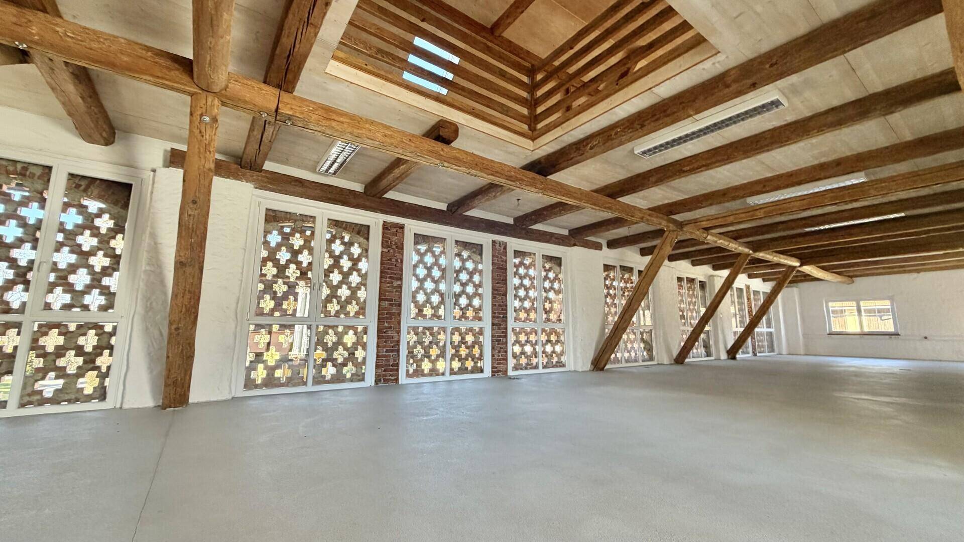 Geräumiger, heller Raum mit sichtbaren Holzbalken und großen Fenstern, bereit zur individuellen Gestaltung.