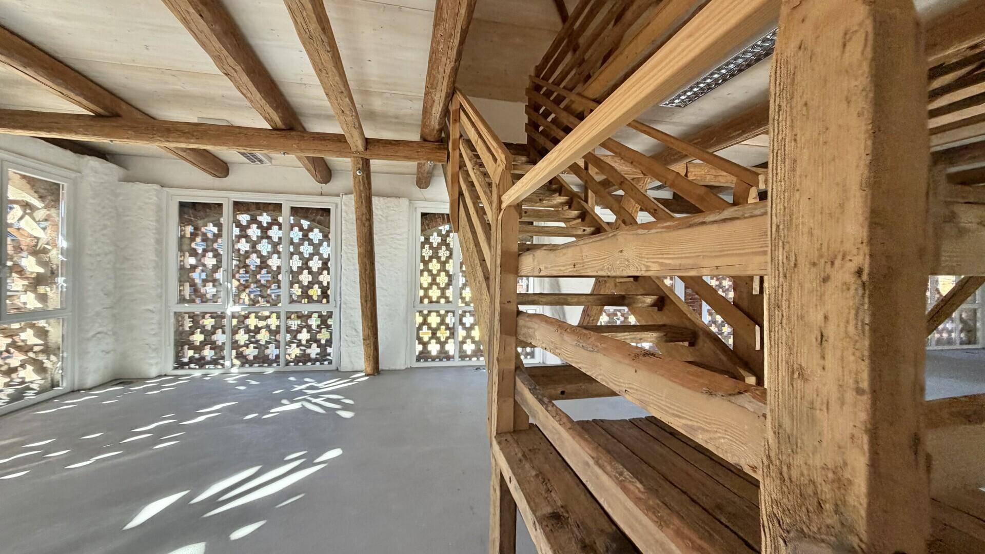 Detailansicht der rustikalen Holztreppe in einem hellen, offenen Raum mit großen Fenstern.