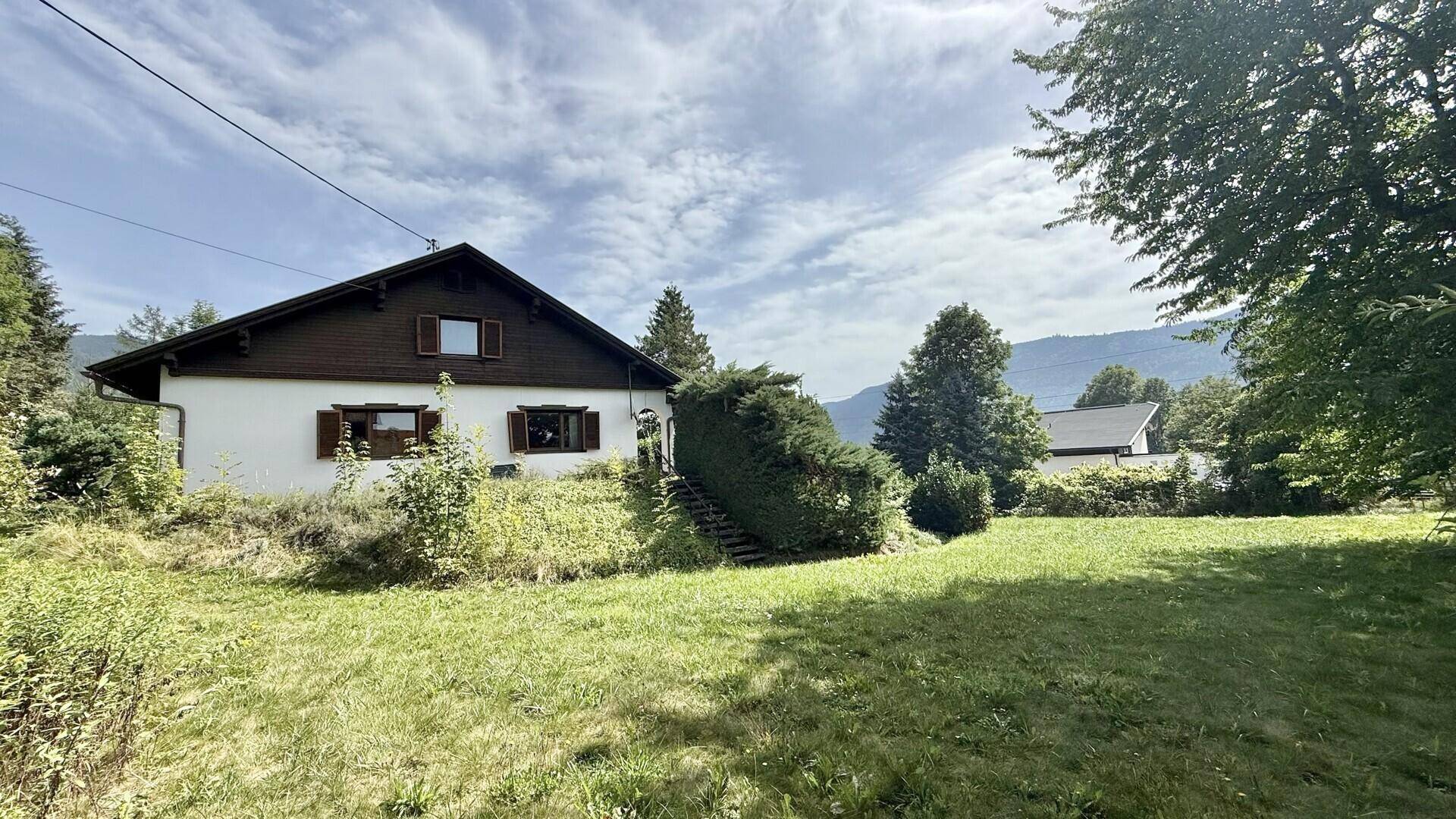 Freistehendes Haus mit Satteldach, weißer Fassade und großem Garten in ländlicher Umgebung.