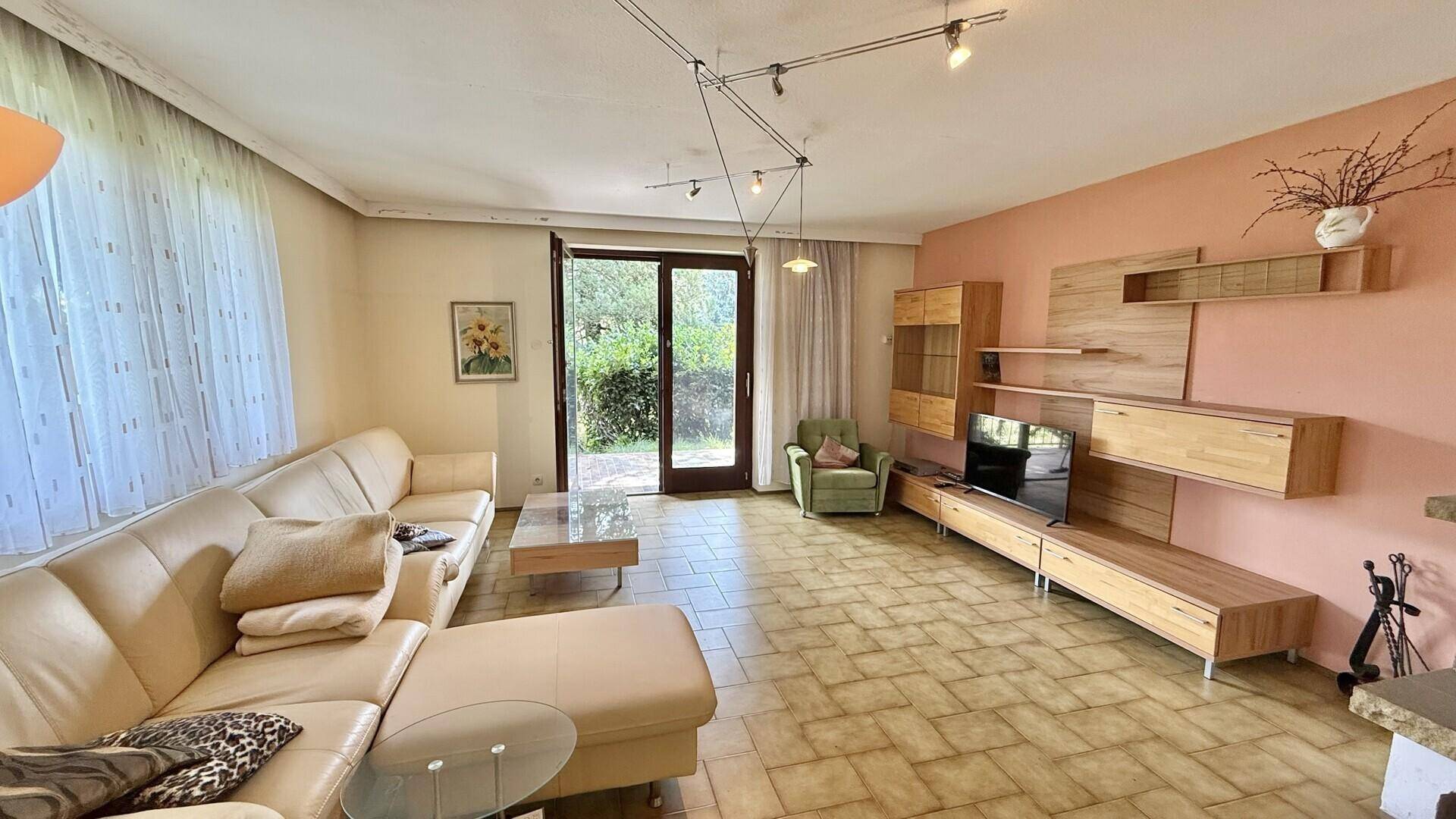Helles Wohnzimmer mit Zugang zur Terrasse und moderner Holz-Wohnwand.