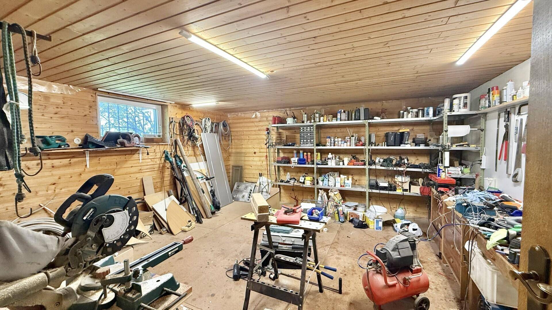 Geräumige Werkstatt mit Holzverkleidung, Regalen voller Werkzeuge und Arbeitsgeräten.