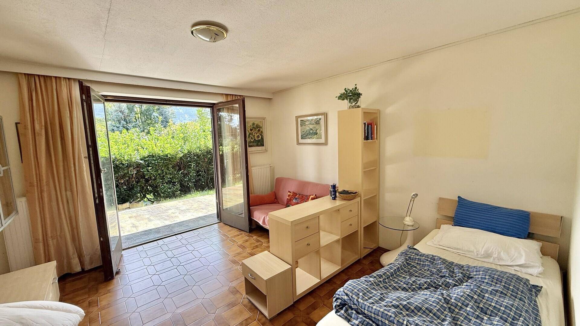 Schlafzimmer mit Einzelbett, Fliesenboden und direktem Zugang zum Gartenbereich.