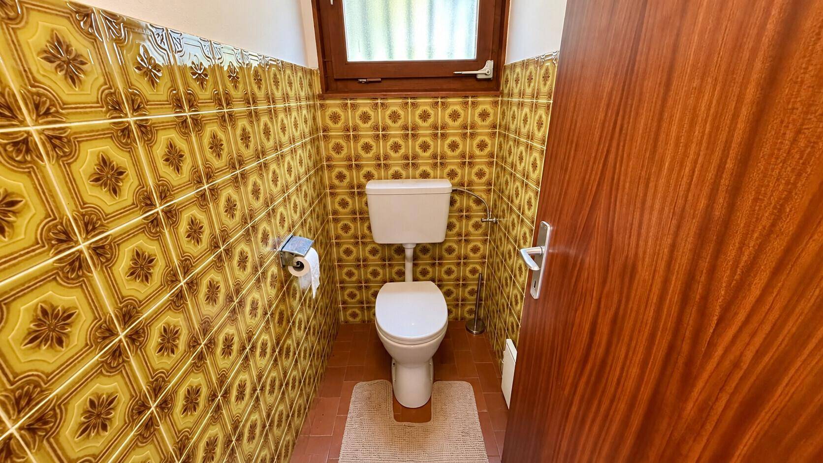 Separate Toilette mit gelb-braunen Fliesen und Fenster, passend zum Stil des Badezimmers.