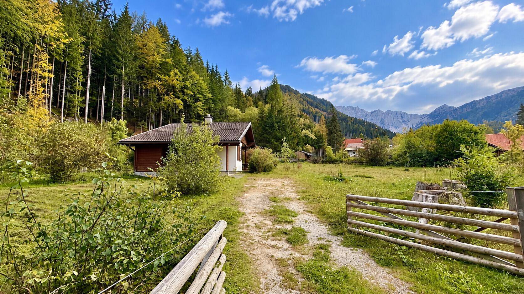 Landhaus mit Holzzaun und Bergpanorama, umgeben von Wiesen und Wäldern.