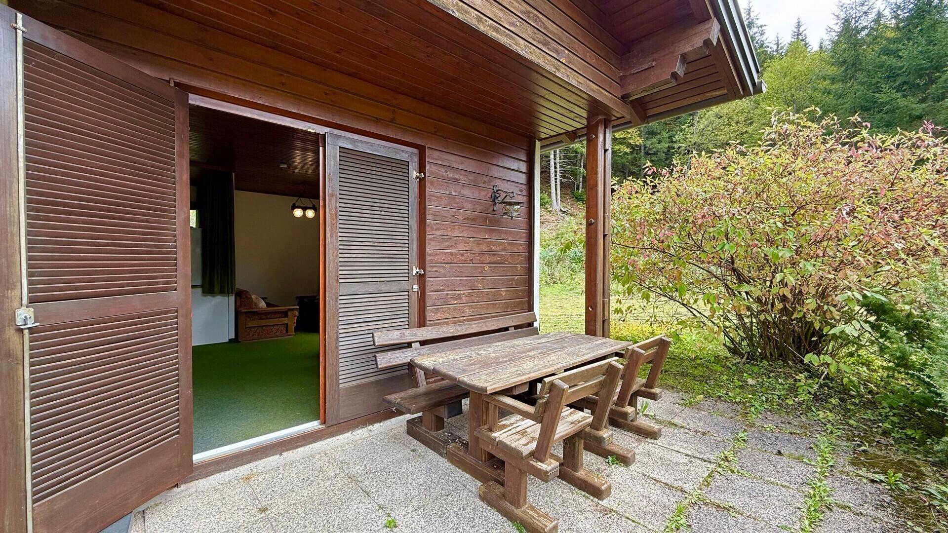 Terrasse mit Holztisch und Zugang zum Wohnbereich, umgeben von üppiger Vegetation.