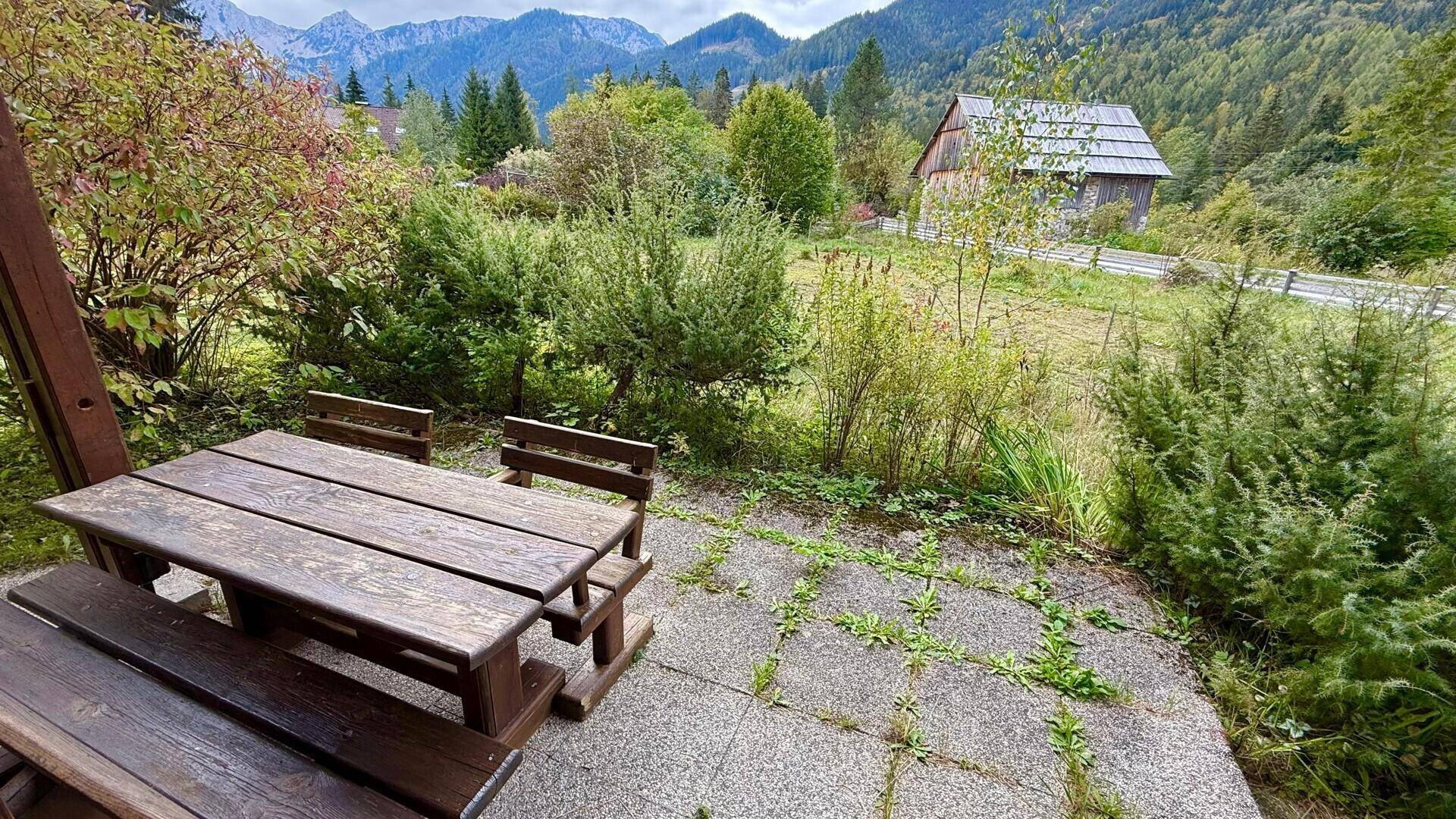 Gemütliche Terrasse mit Holztisch und Bänken, umgeben von Natur und Bergblick.