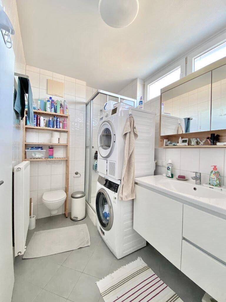 Modernes Badezimmer mit Dusche, WC, Waschbecken und integrierter Waschmaschine und Trockner.