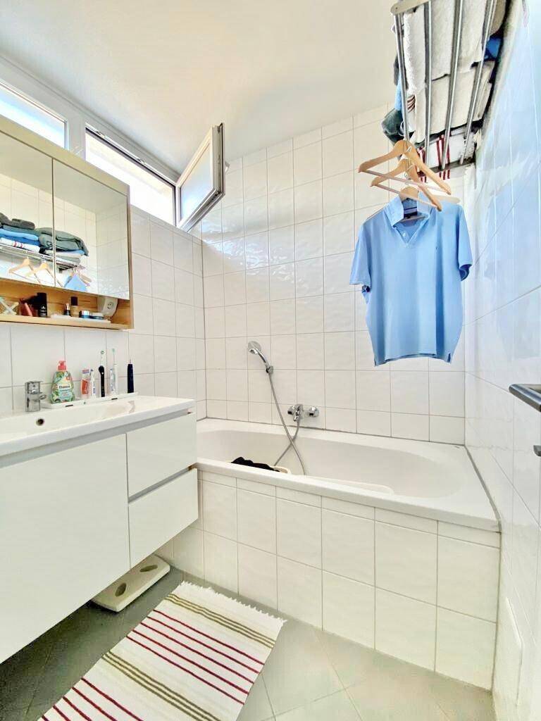 Helles Badezimmer mit Badewanne, Waschbecken und Spiegelschrank, komplett gefliest.