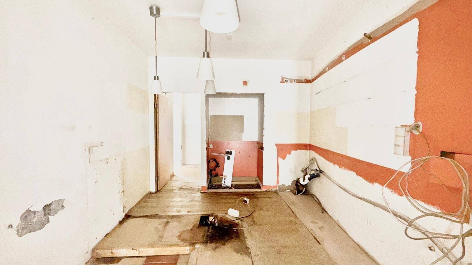 Renovierungsbedürftiger Innenraum mit teilweise entfernten Böden, sichtbaren Kabeln und roten Farbakzenten.