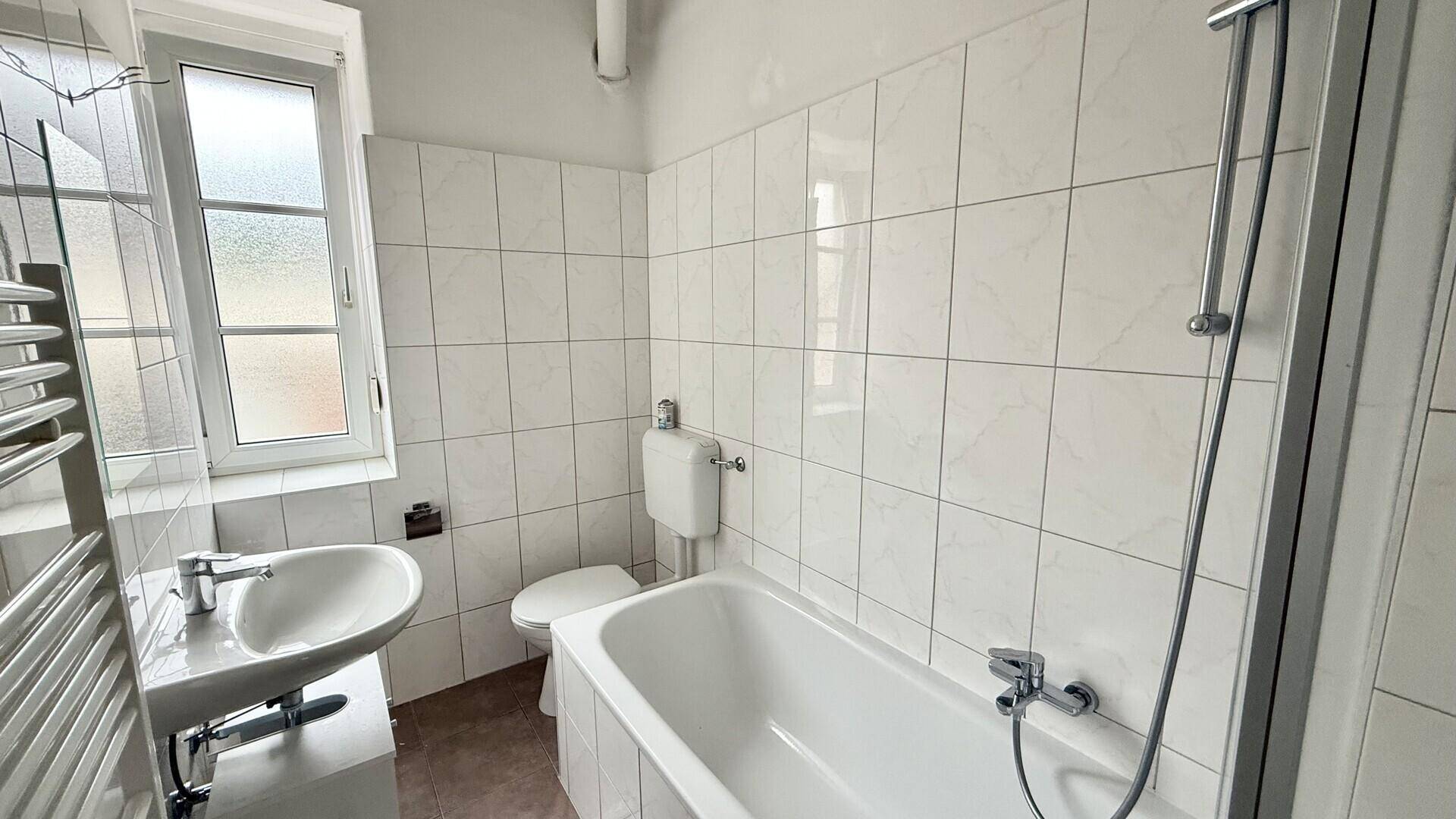 Modernisiertes Badezimmer mit weißen Fliesen, Badewanne mit Dusche und beheiztem Handtuchhalter.