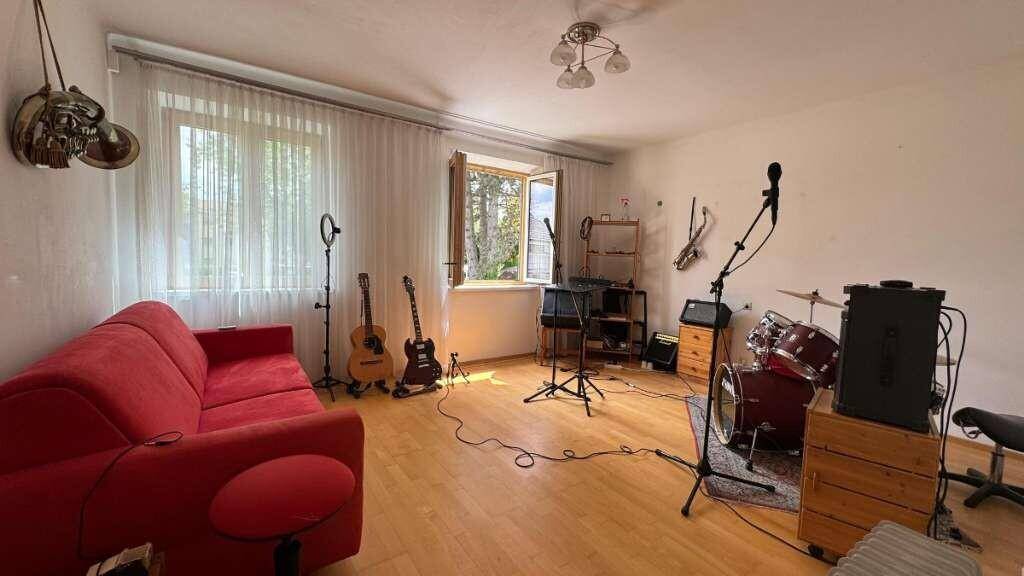 Vielseitiger Raum mit Musikinstrumenten, rotem Sofa und Holzboden, ideal für Hobbys.