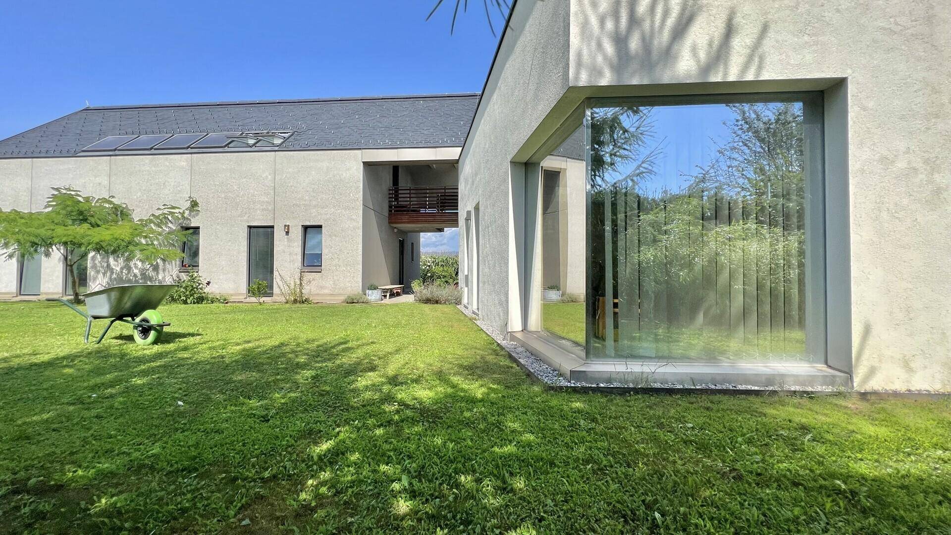 Modernes Wohnhaus mit großen Fenstern und gepflegtem Garten unter strahlend blauem Himmel.