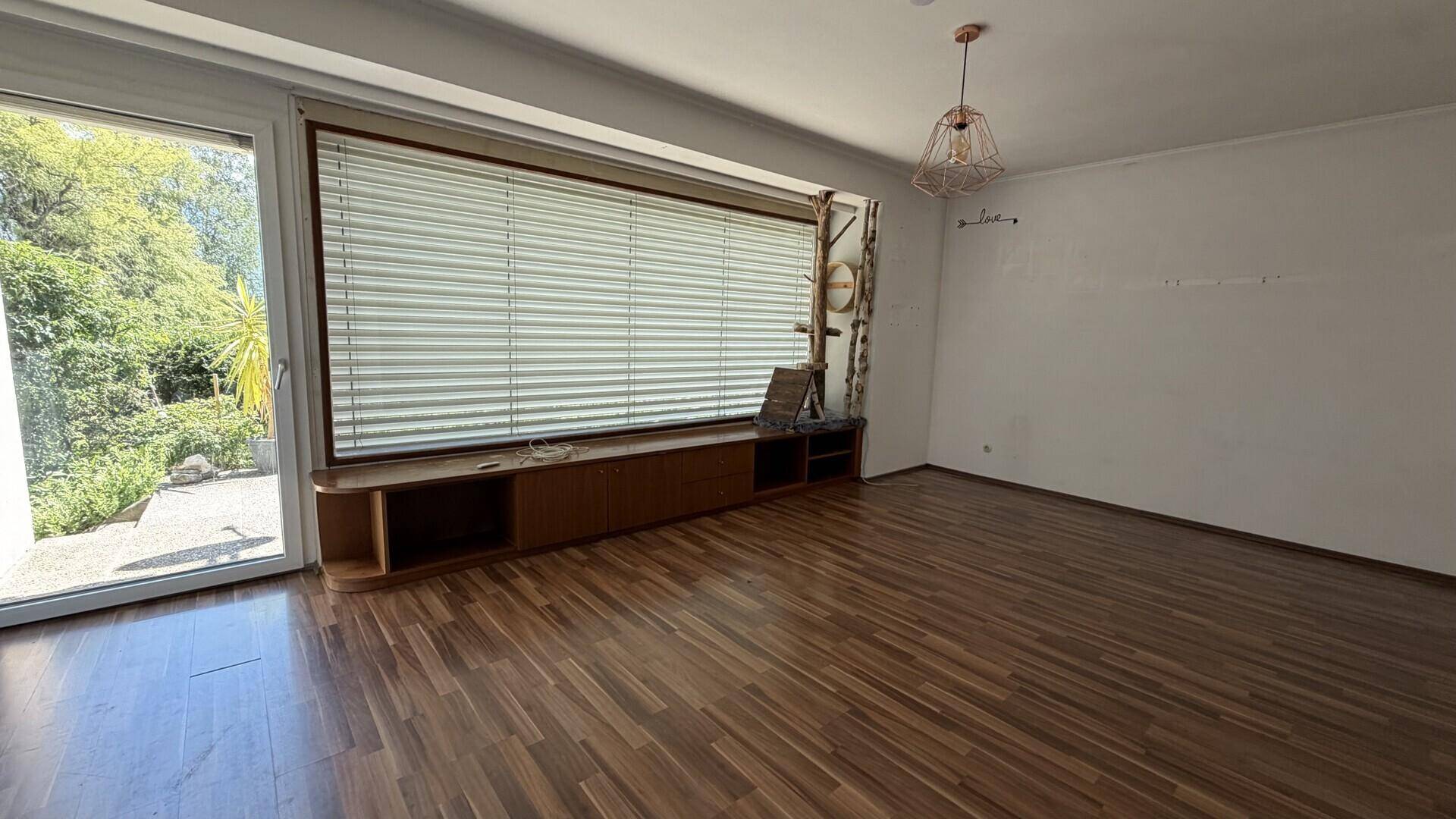Helles Wohnzimmer mit Holzboden, großen Fenstern und Blick ins Grüne.